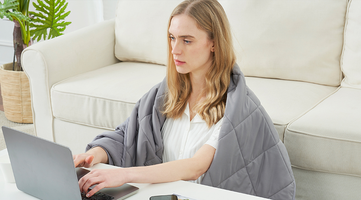 Woman working on a laptop while wrapped in a gray cooling blanket.