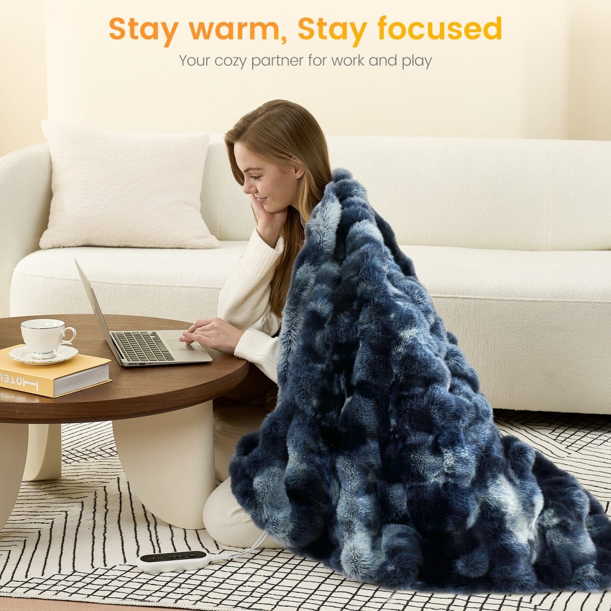Woman using a laptop on a coffee table with a tie-dye blue faux fur heated electric throw blanket draped over her, sitting on the floor in a cozy living room. #color_Tie-dye Blue