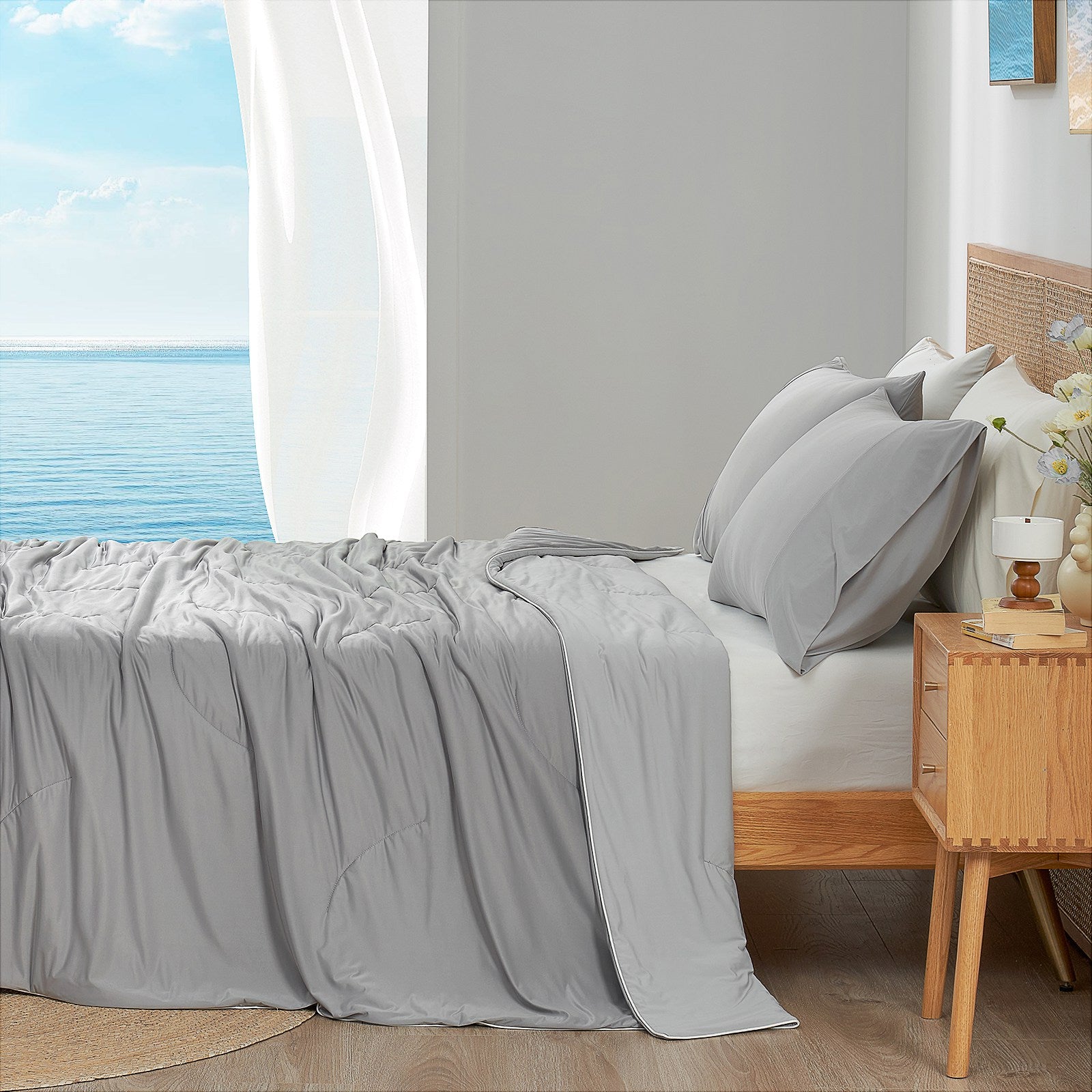 Cool Grey cooling comforter on bed side view with sea, offering breathable bedding for a cozy sleep. #color_Cool Grey