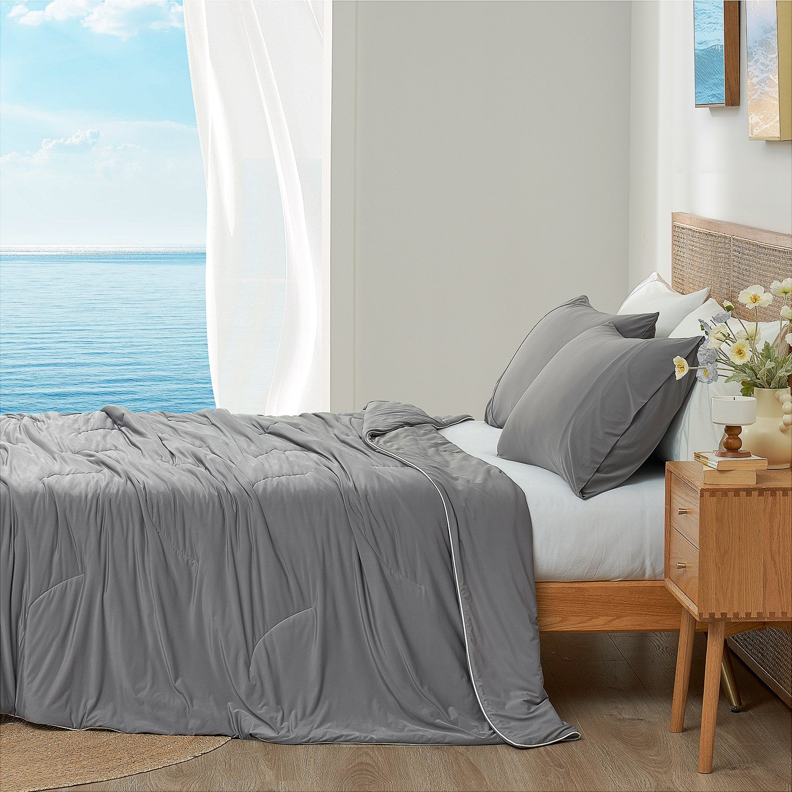 Dark grey cooling comforter on bed side view with sea, offering breathable bedding for a cozy sleep. #color_Dark Grey