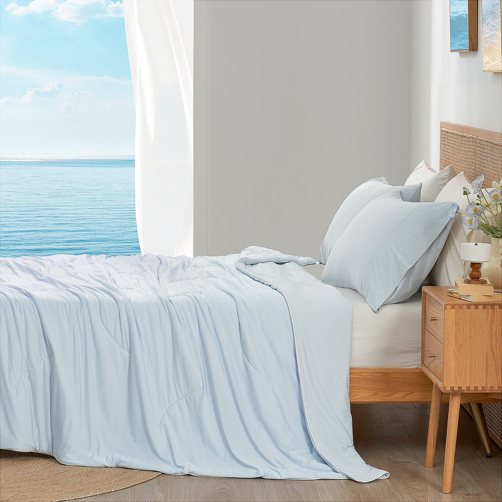 Cool blue cooling comforter on bed side view with sea, offering breathable bedding for a cozy sleep. #color_Cool Blue