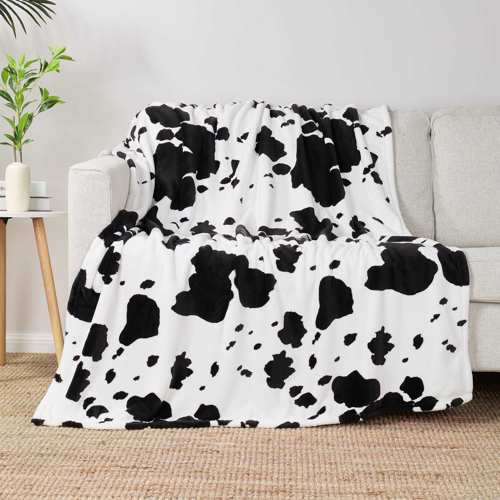 Cow print throw blanket on a sofa, cozy home decor. Soft, breathable blanket for comfort. #color_Black White