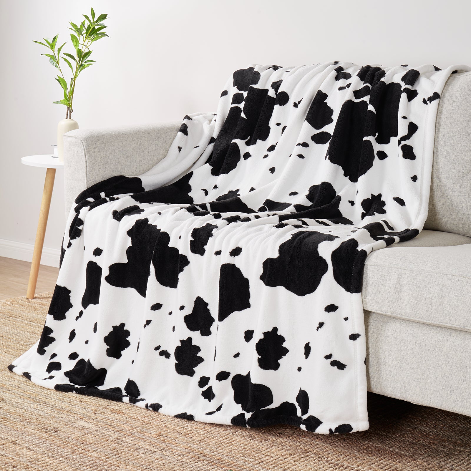Black and white cow print blanket draped over a sofa in a living room setting. #color_Black White