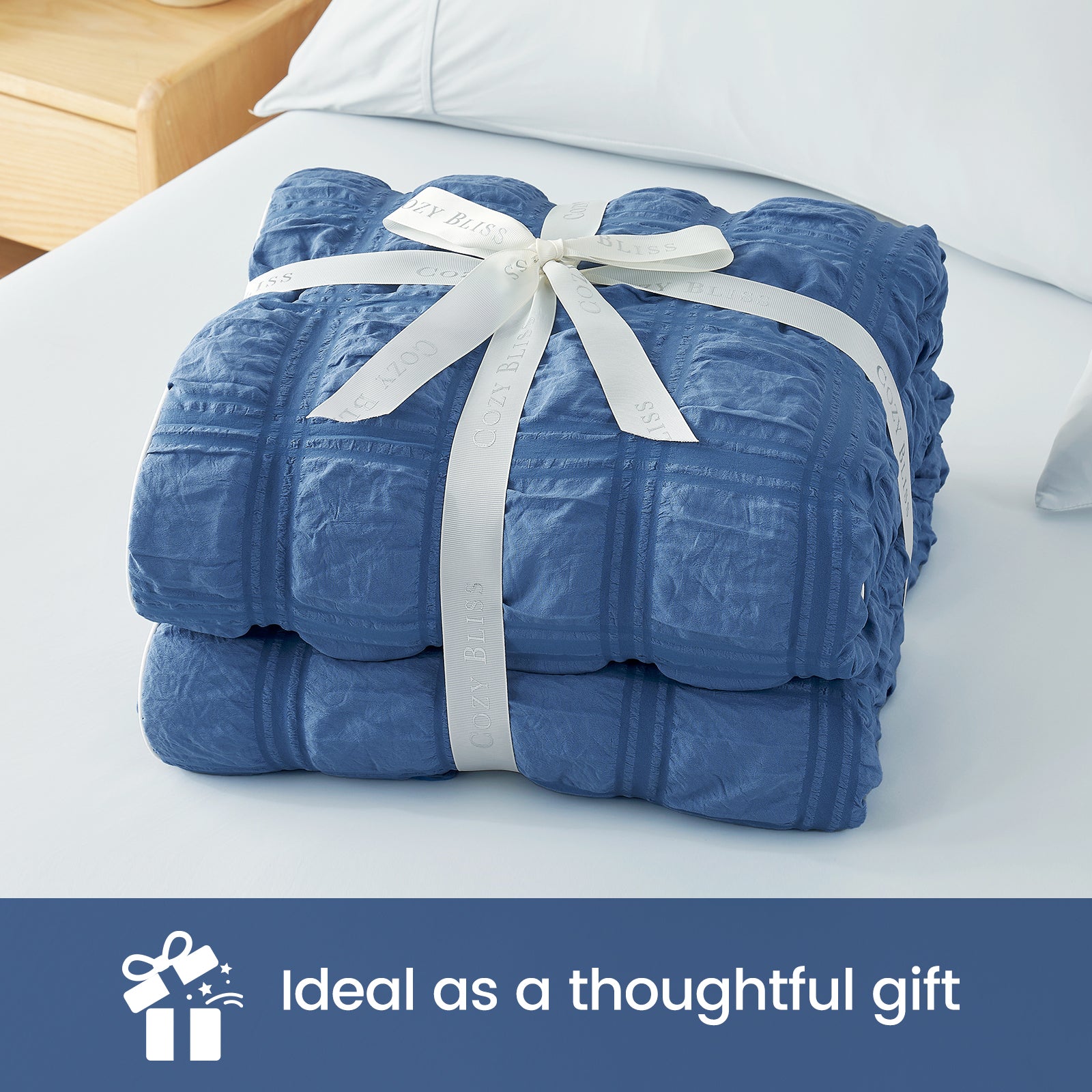 Blue quilt with a white ribbon on a bed, labeled as an ideal gift. #color_Denim Blue