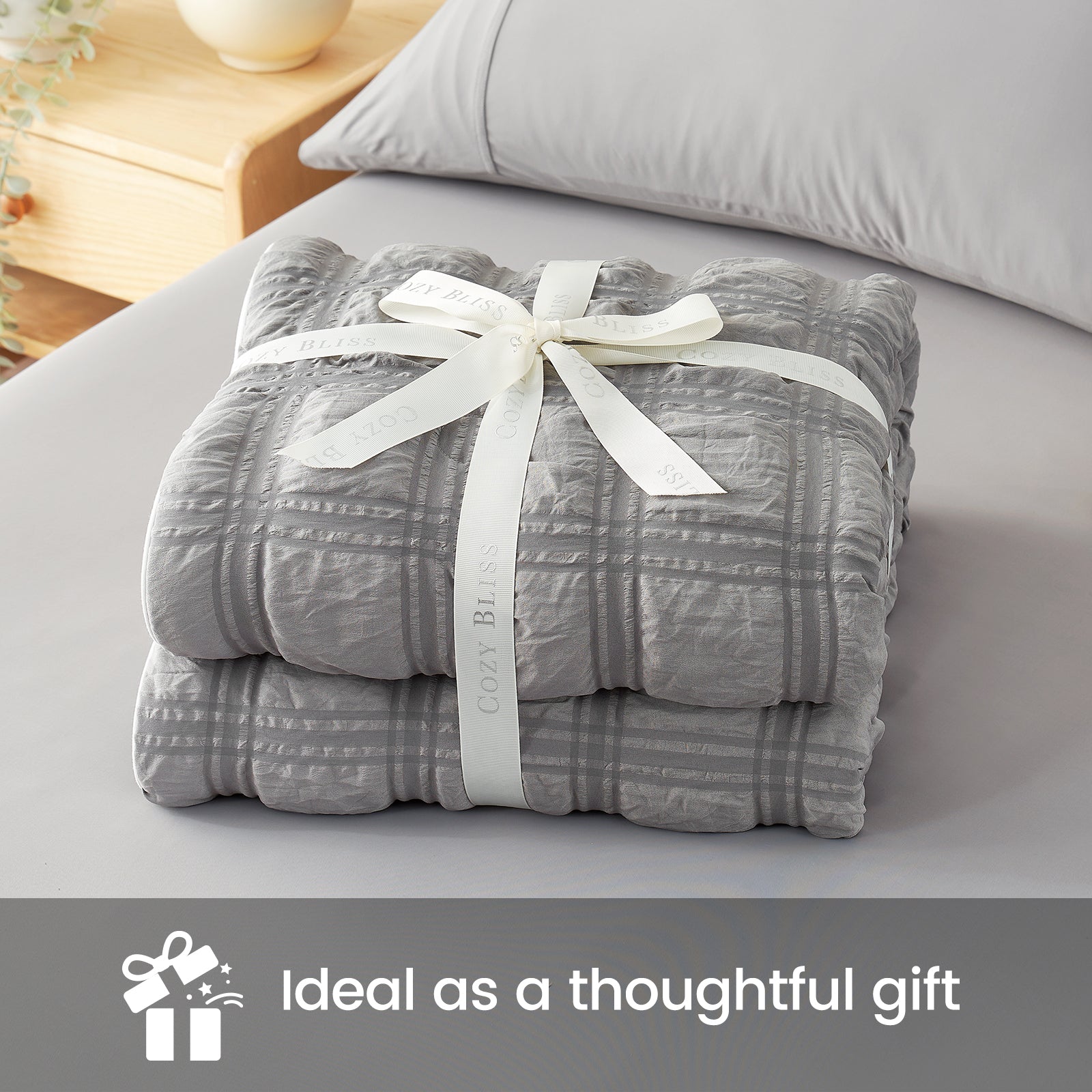Folded gray blanket with a white ribbon on a bed, labeled as a thoughtful gift. #color_Dark Gray