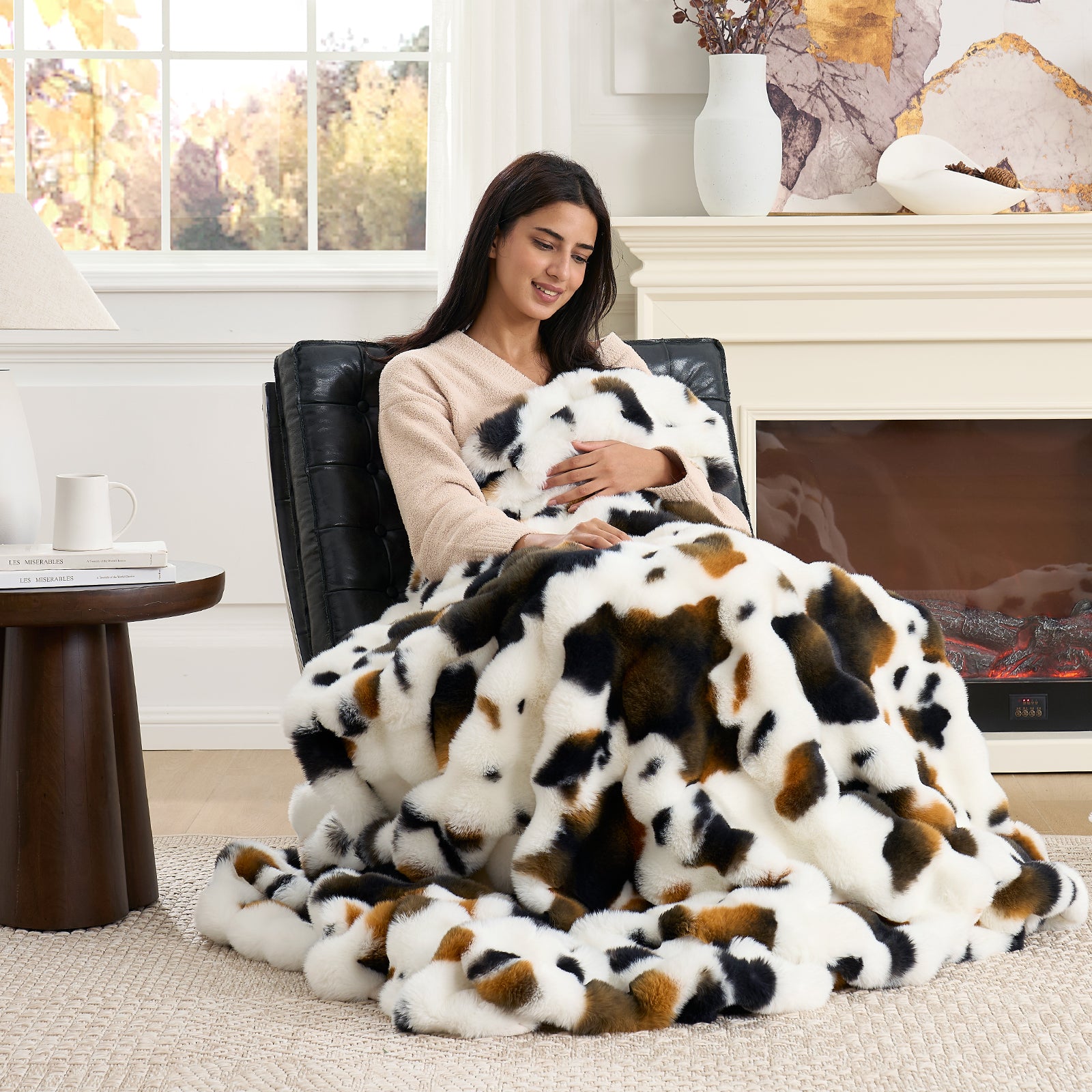 Woman sitting in a chair with a cow patterned blanket, surrounded by home decor elements. #Color_Cow