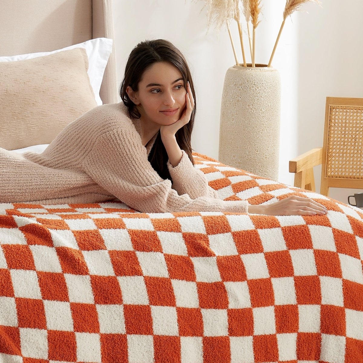 Woman relaxing on a bed with a Checkered Feather Yarn Knit Throw Blanket in Burnt Orange in a cozy home setting. #Color_Burnt Orange