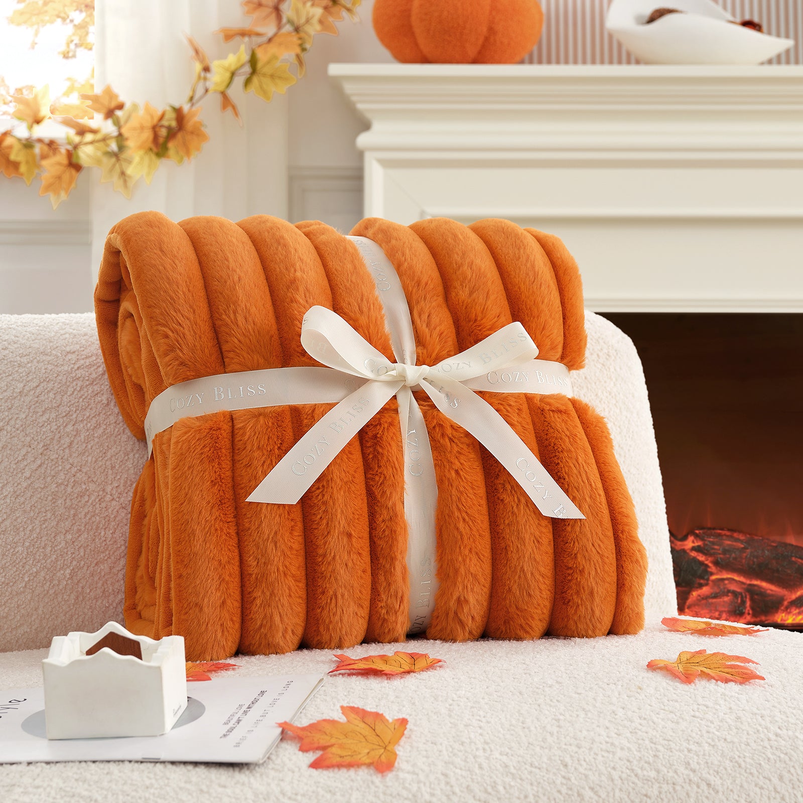 Orange blanket with a white ribbon tied around it, placed on a couch in front of a fireplace. #color_Burnt Orange