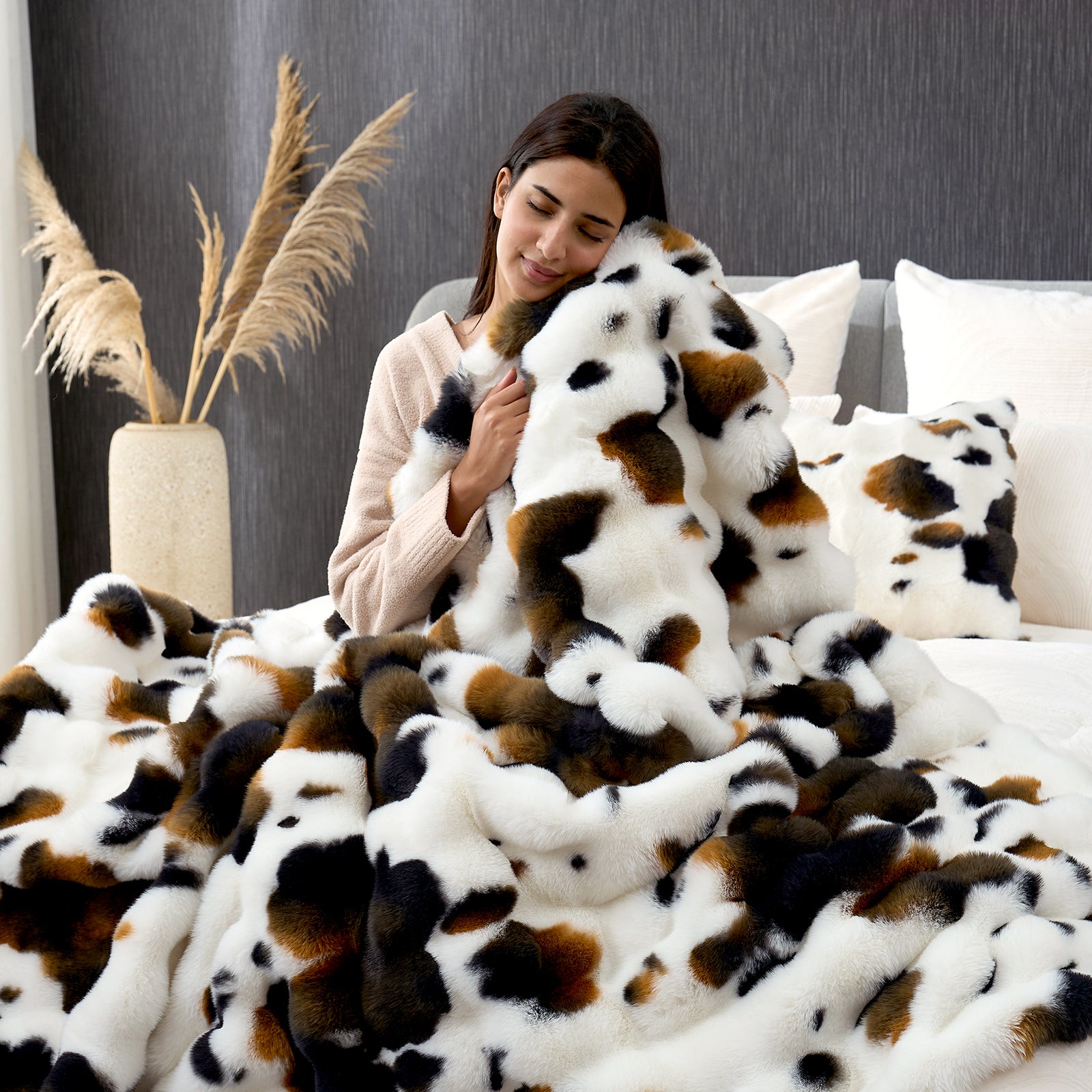 Woman hugging a fluffy, multicolored blanket on a bed with a neutral background#Color_Cow