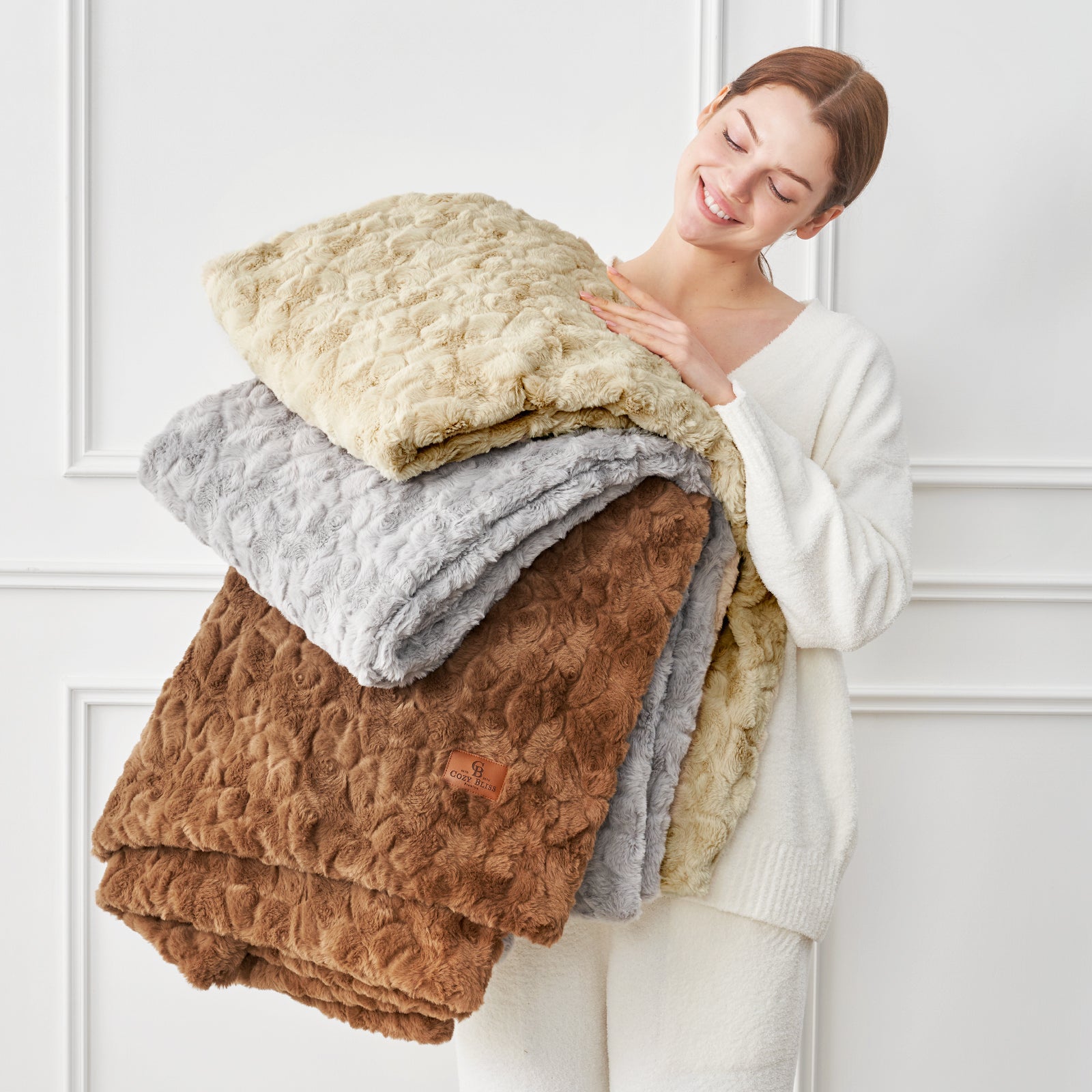 Woman holding a stack of folded blankets against a white wall#color_Tie-dye Khaki