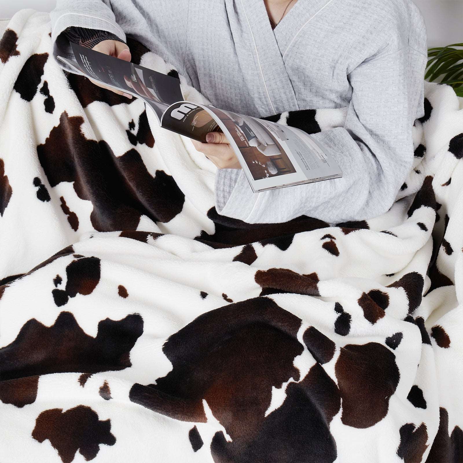 Person relaxing under a cozy blanket, featuring a cow print, reading a magazine #color_Black Brown