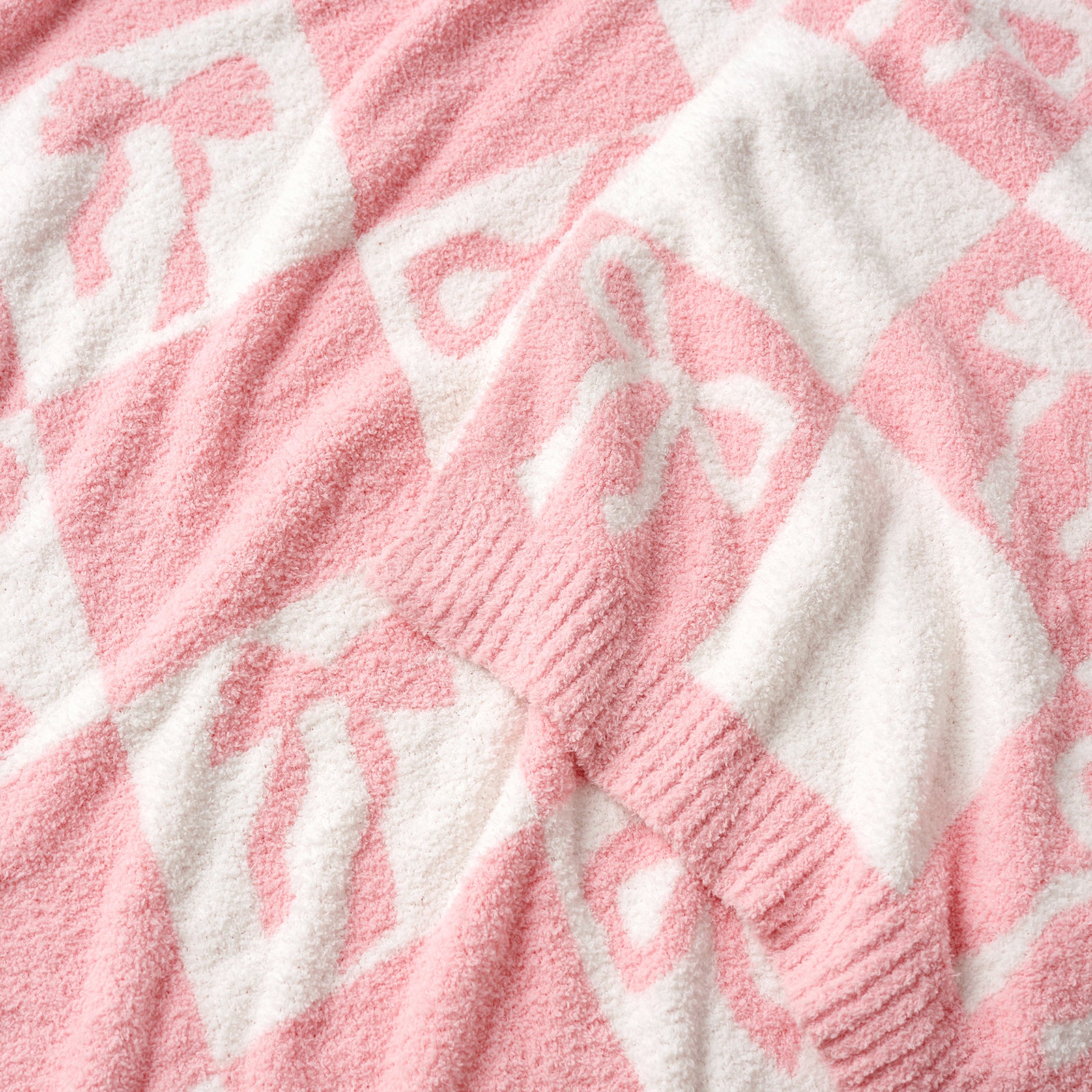 Close-up of Reversible Checkered Bow Feather Yarn Throw Blanket in Pink showcasing plush feather yarn texture, bow pattern and knit edging detail. #color_Pink