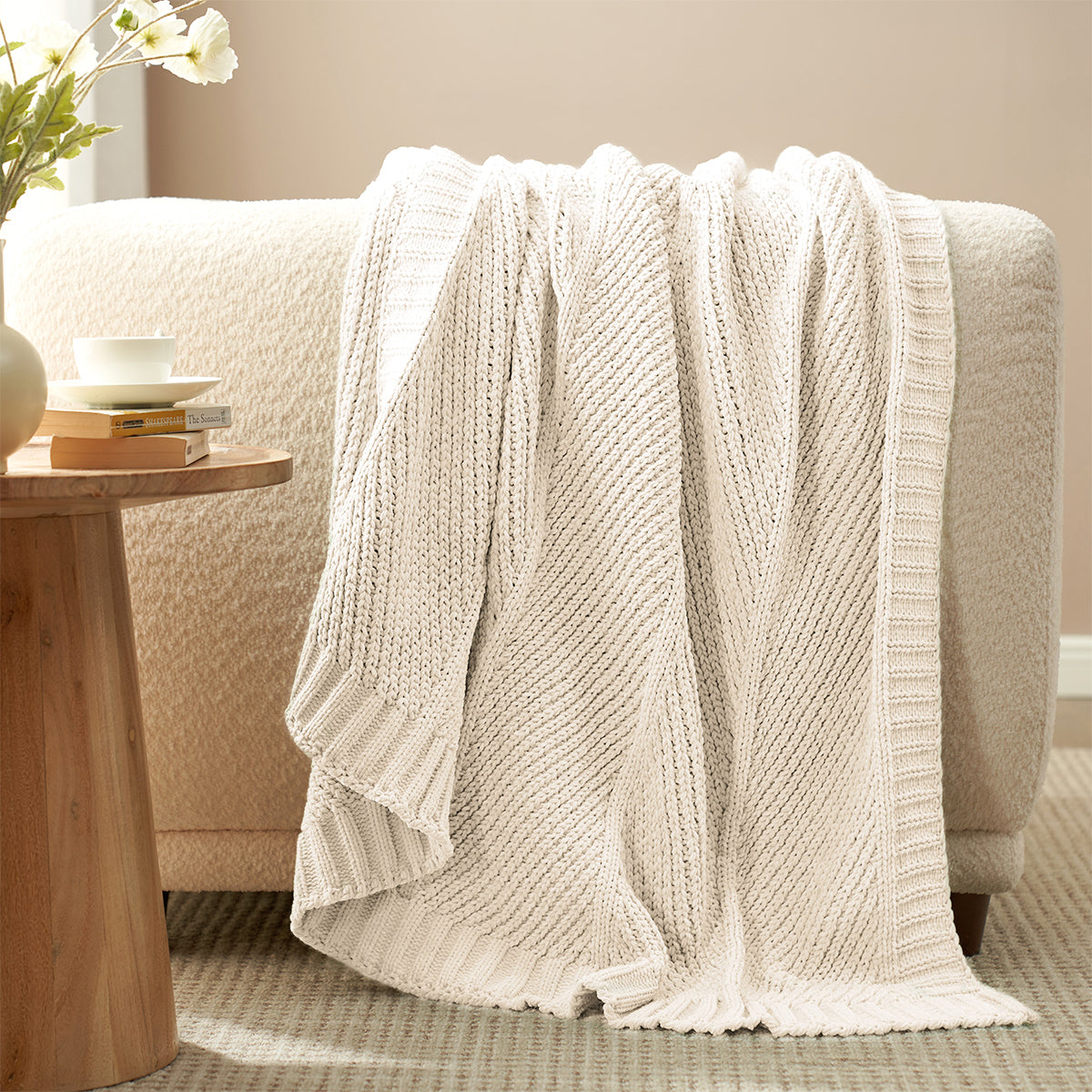 Chevron Chenille Knit Throw Blanket in Ivory draped over a sofa, showcasing its soft chenille texture and elegant chevron knit design. #color_Ivory