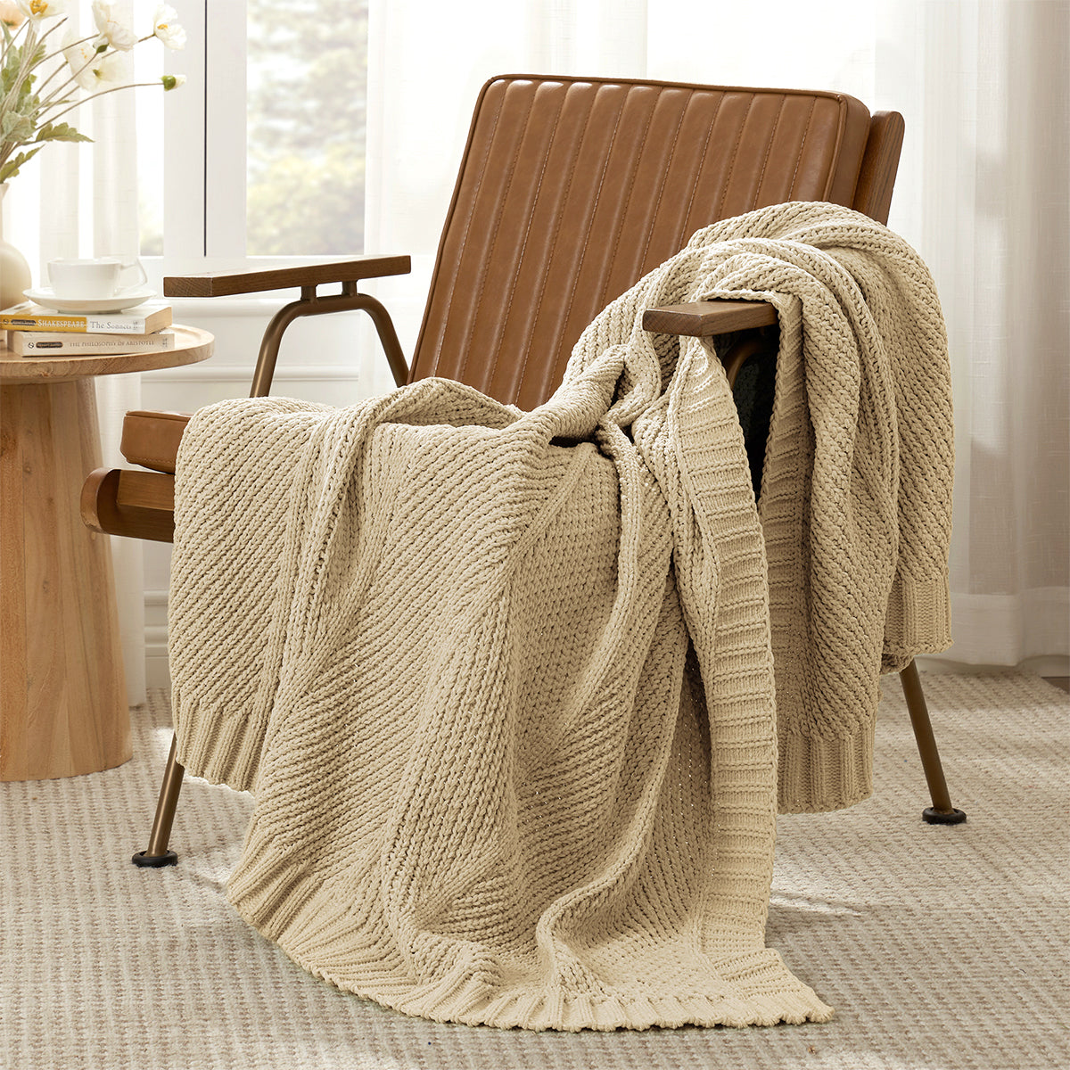 Ivory knitted blanket draped over a beige armchair in a room with a table and window. #color_Beige
