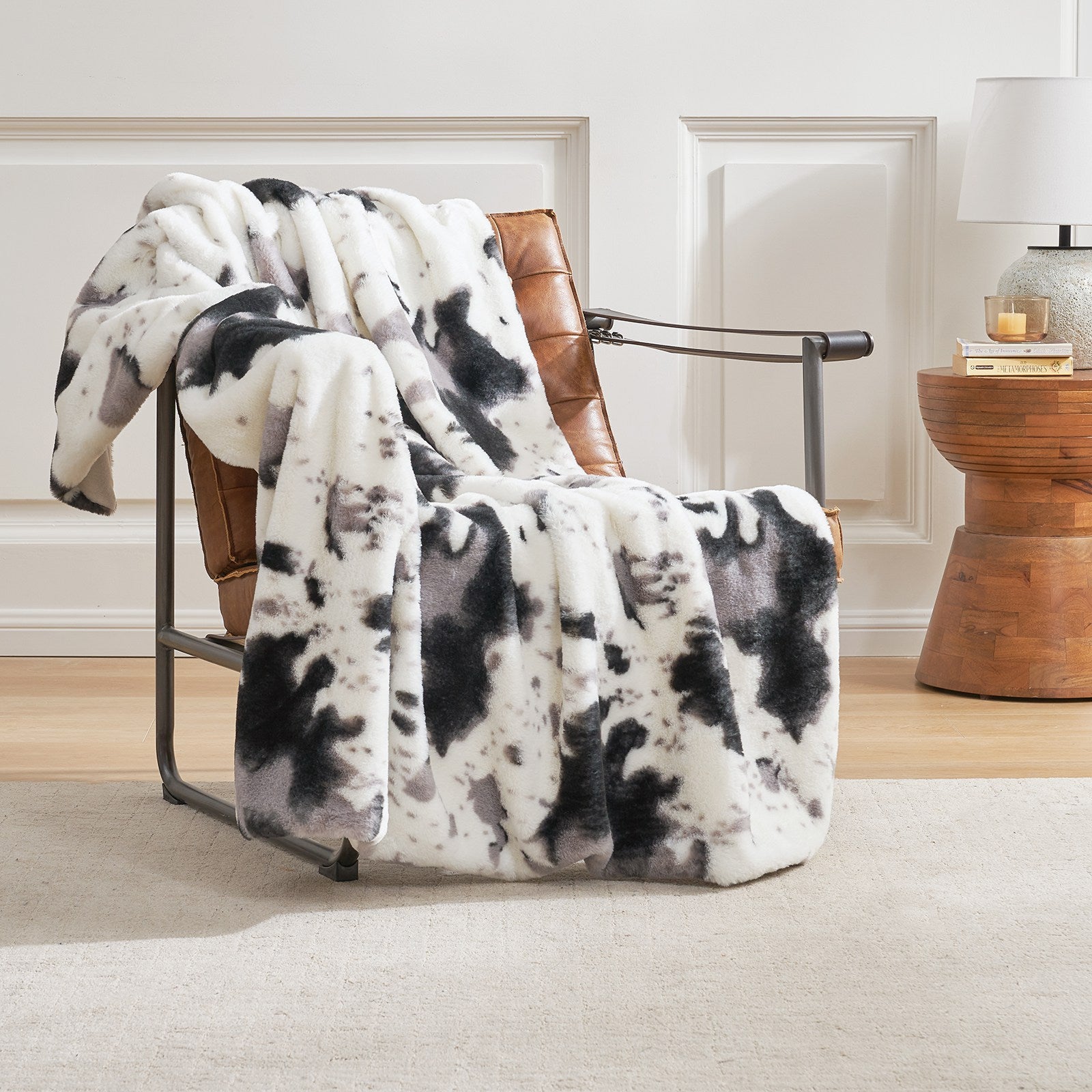 Cow print faux fur throw blanket draped over a chair, cozy bedding #color_Black/Grey