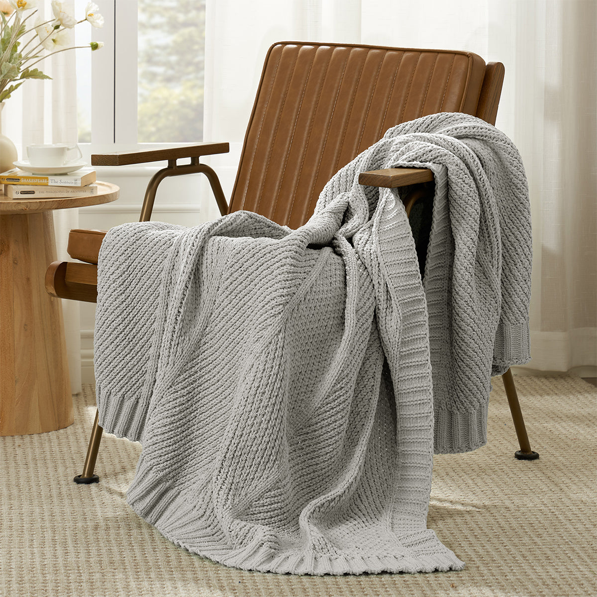 Ivory knitted blanket draped over a light grey armchair in a room with a table and window. #color_Light Grey