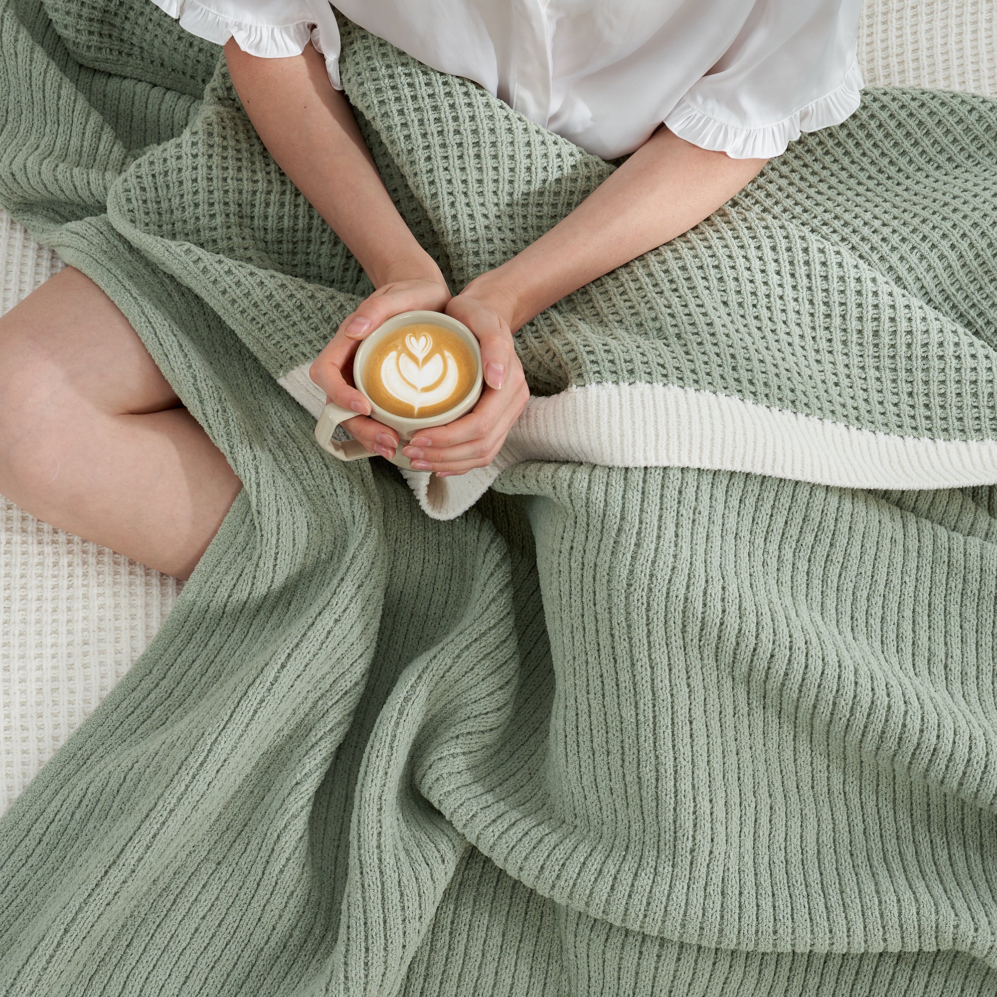 Woman wrapped in a Chenille Waffle Knit Throw Blanket in Sage Green, enjoying a cup of coffee. #color_Sage Green
