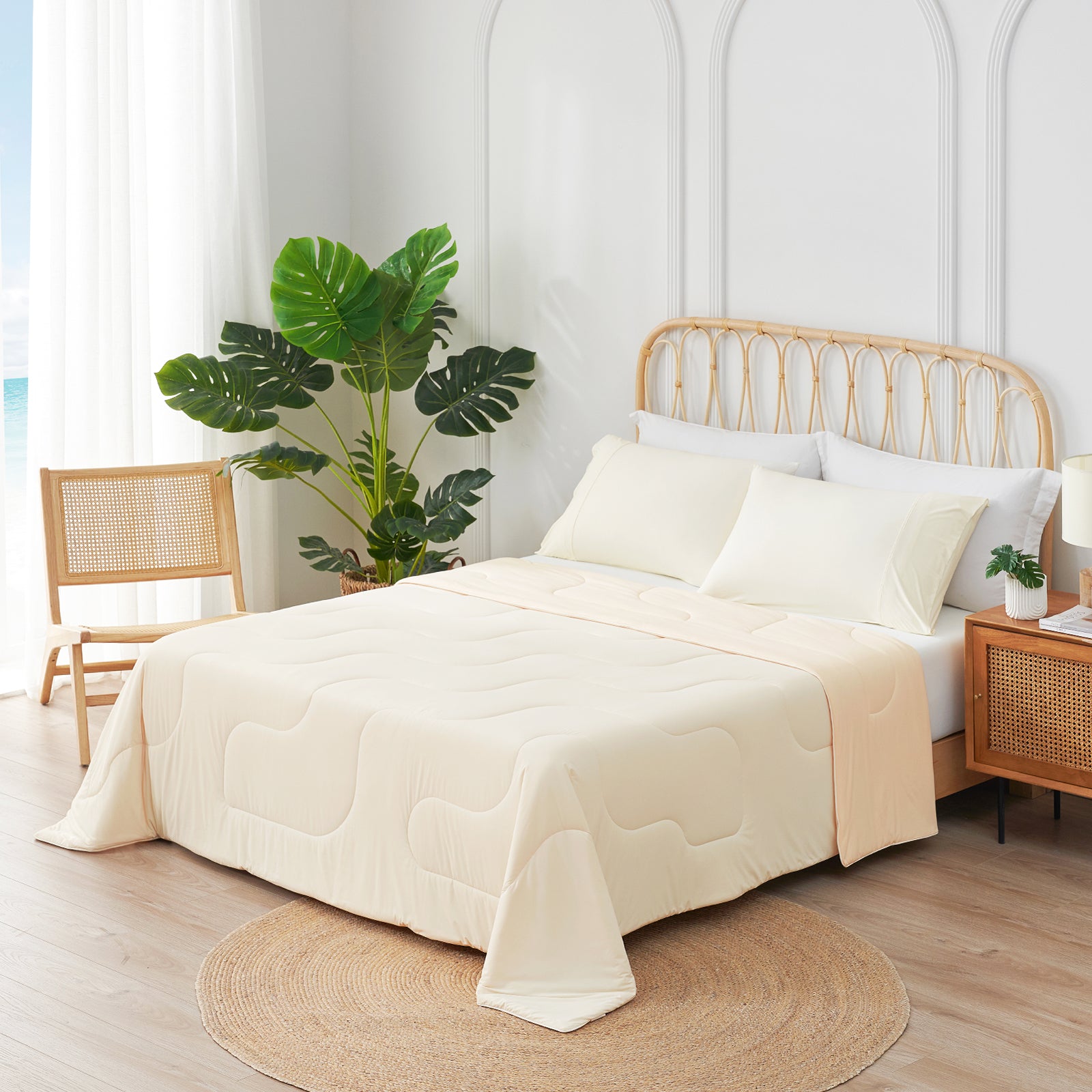 Bedroom with a bed covered in a beige comforter, white pillows, and a wooden headboard. There is a plant and a chair in the room. #Color_Cream White