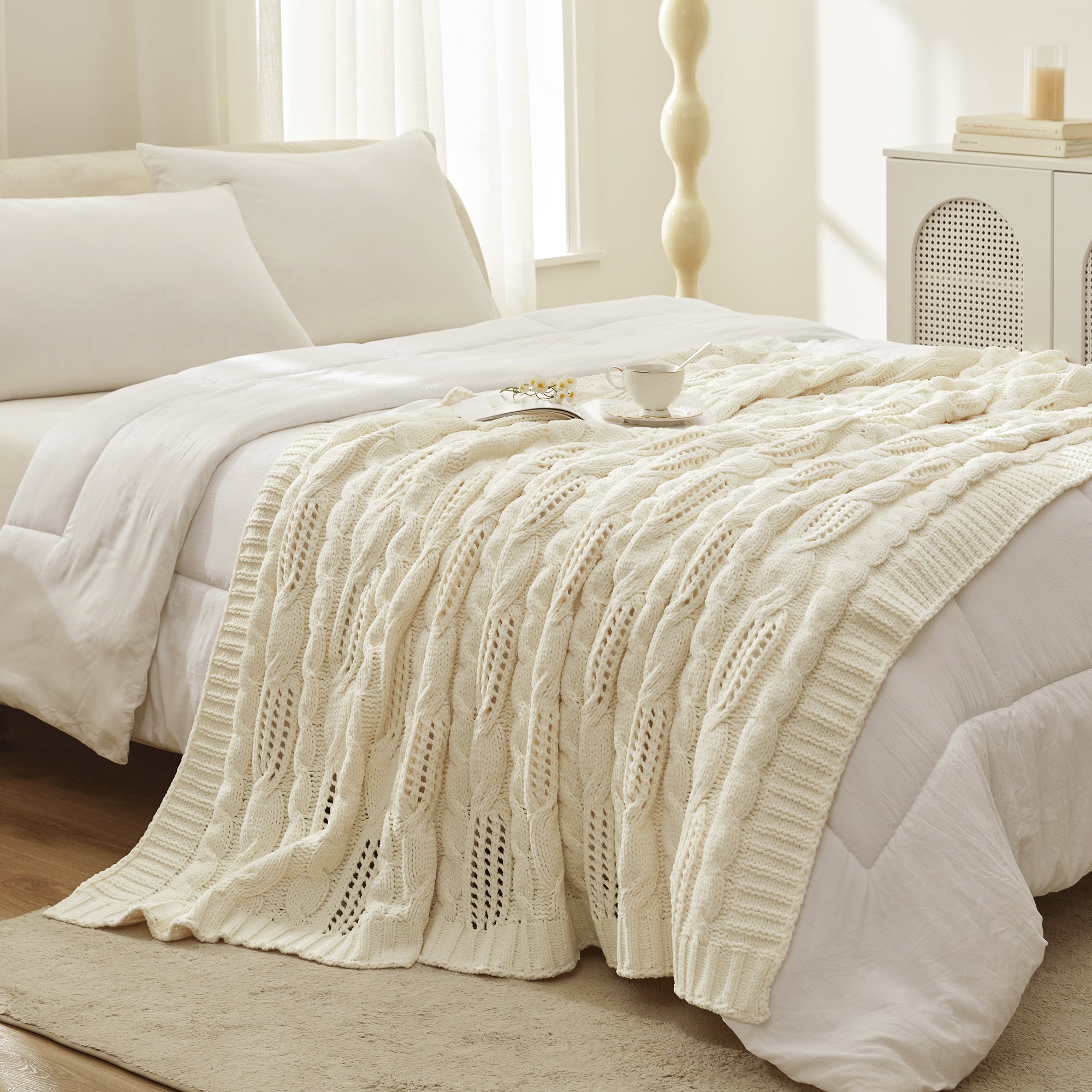 Chenille Cable Knit Throw Blanket in Ivory styled on a bed in a bright bedroom, adding a clean and cozy layered look. #color_Ivory
