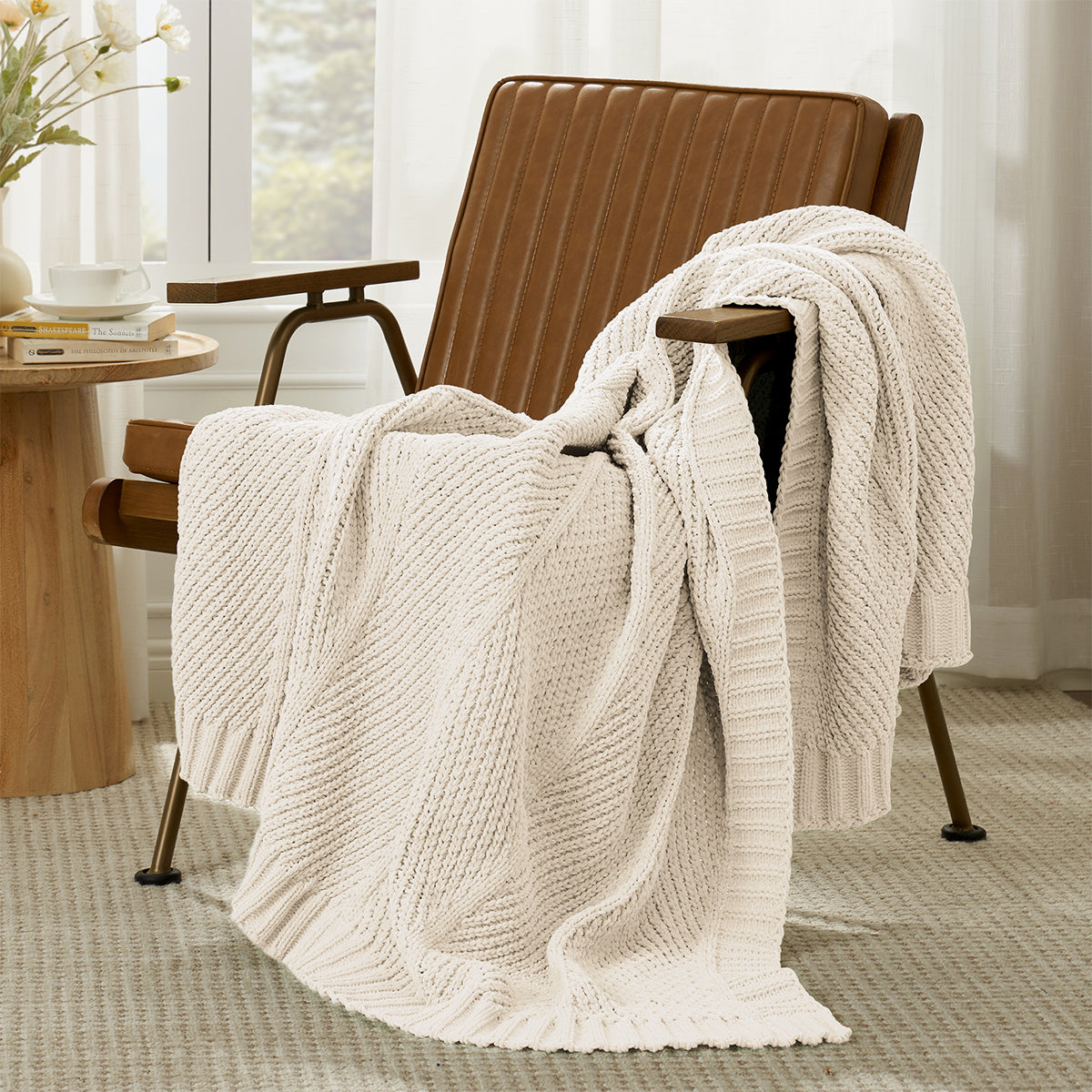 Ivory knitted blanket draped over a brown armchair in a room with a table and window. #color_Ivory