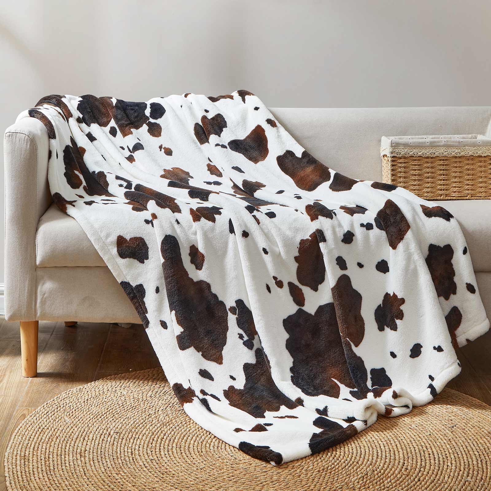 Cow print throw blanket draped over a sofa, featuring soft, breathable MilkyPlush fabric for cozy comfort. #color_Black Brown