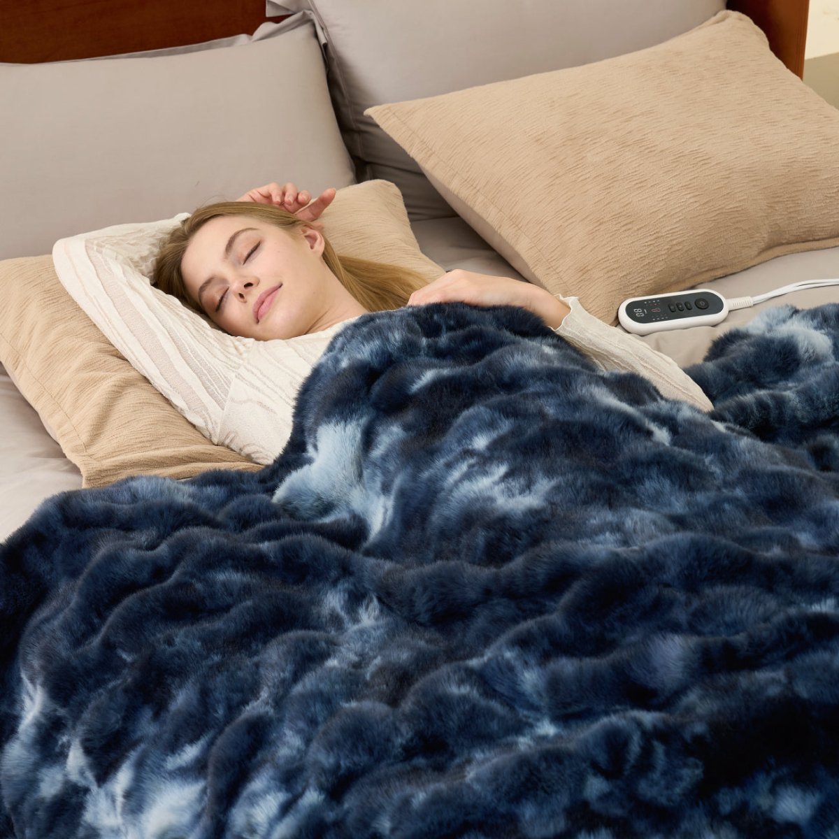 Woman sleeping under a tie-dye blue heated electric blanket with a remote control on a bed. #color_Tie-dye Blue