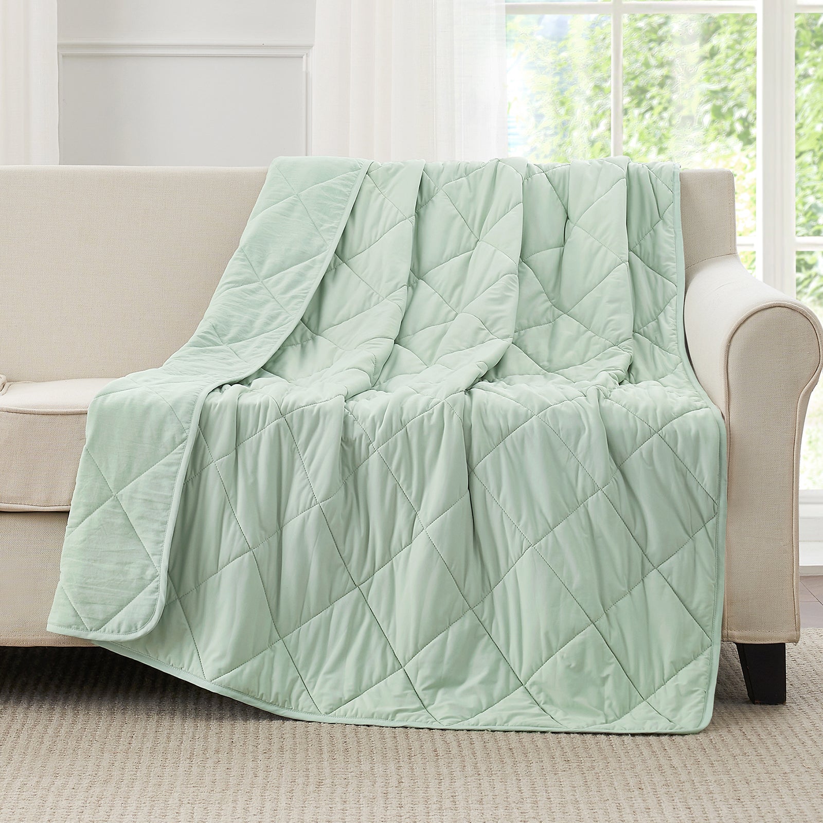 Light green quilt draped over a beige sofa in a bright room with large windows. #color_Mint Green