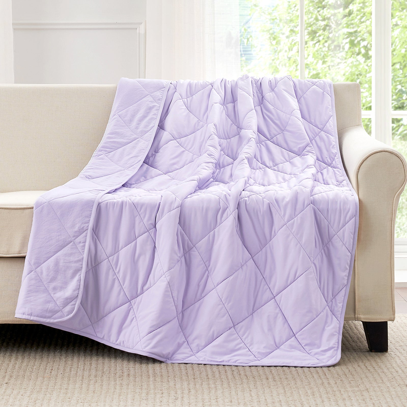 Purple quilted blanket draped over a beige sofa in a room with large windows. #color_Purple