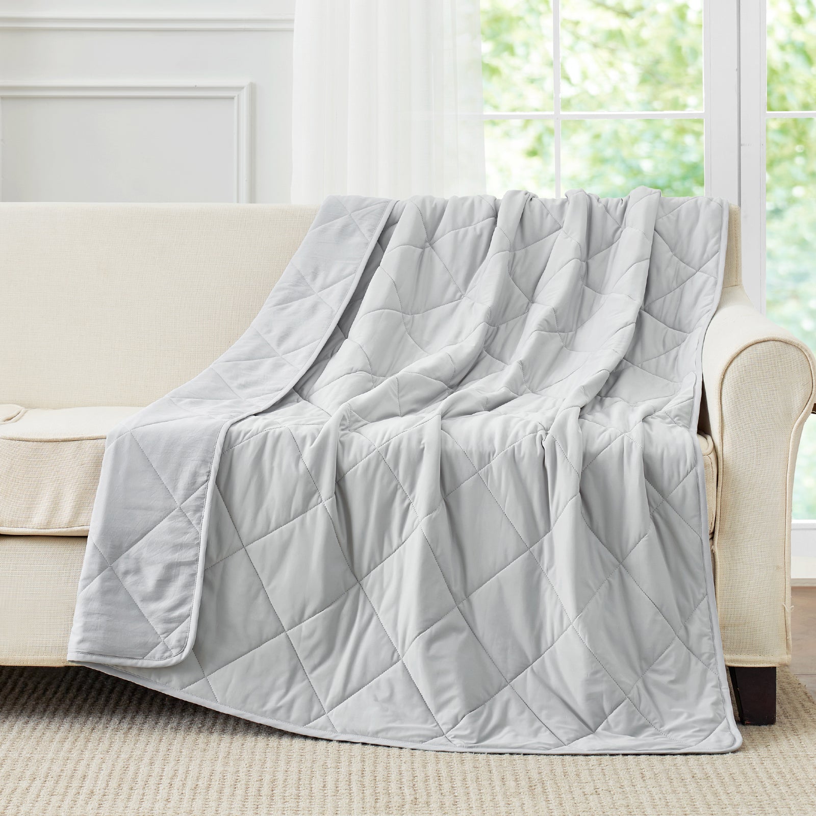 Light grey cooling blanket draped over a beige sofa. #Color_Cool Grey
