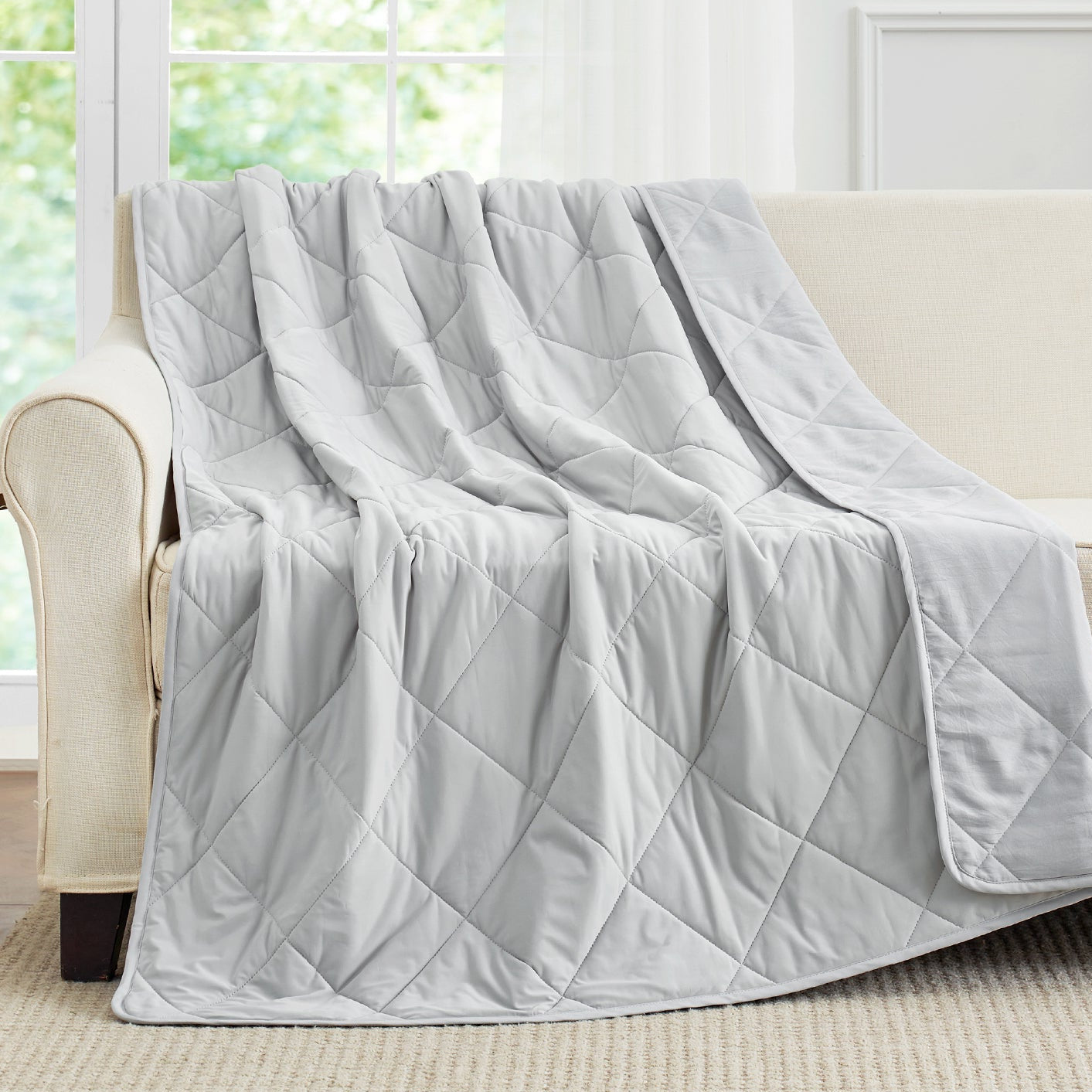Light grey cooling blanket draped over a beige sofa. #Color_Cool Grey