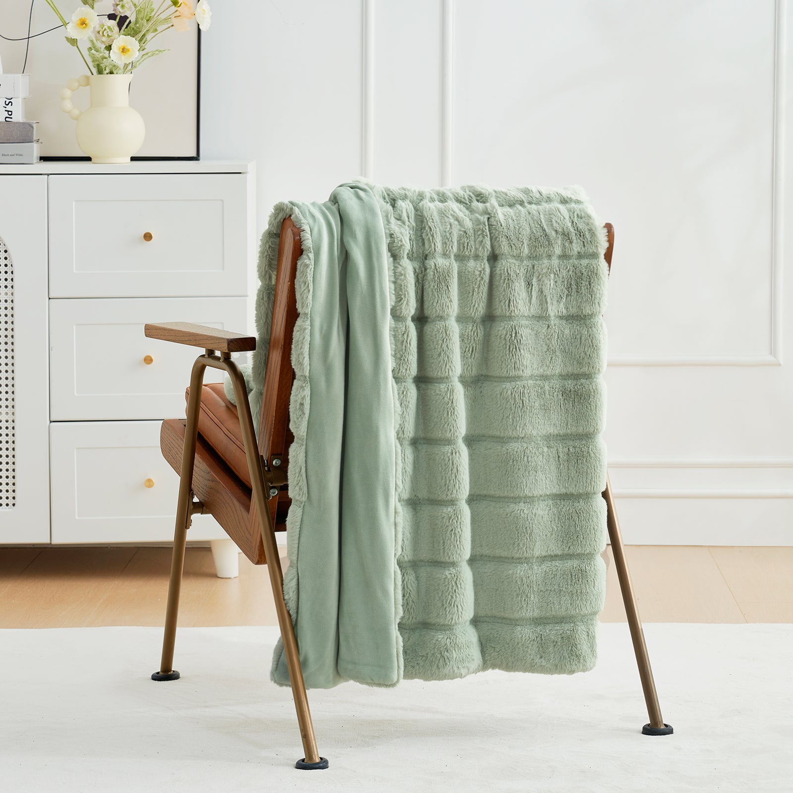 Green textured blanket draped over a wooden chair in a room with white walls and a dresser. #color_Sage Green