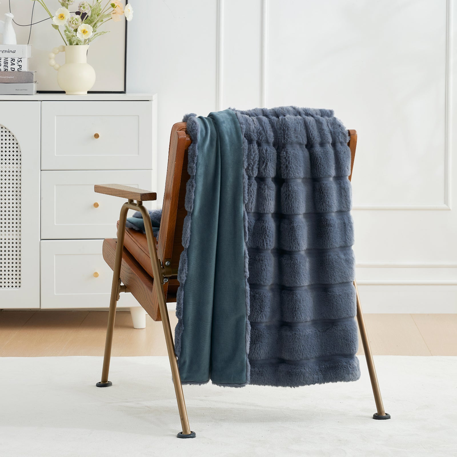 Blue textured blanket draped over a wooden chair in a room with white walls and a dresser. #color_Blue