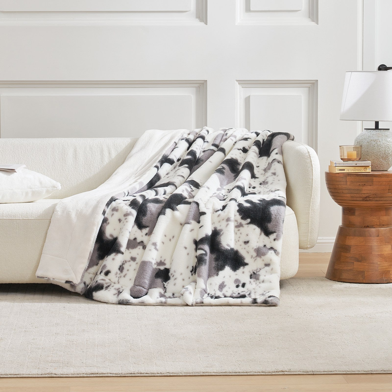 Cow print faux fur blanket draped on a white sofa, a cozy bedding for home decor #color_Black/Grey Cow