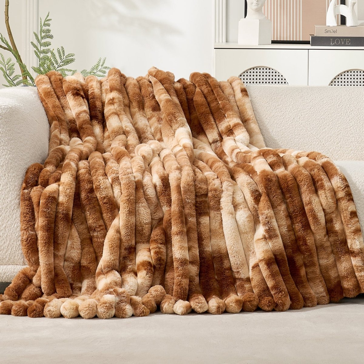 Brown and beige fuzzy blanket draped over a white sofa with a neutral background. #Color_Tie-dye Brown