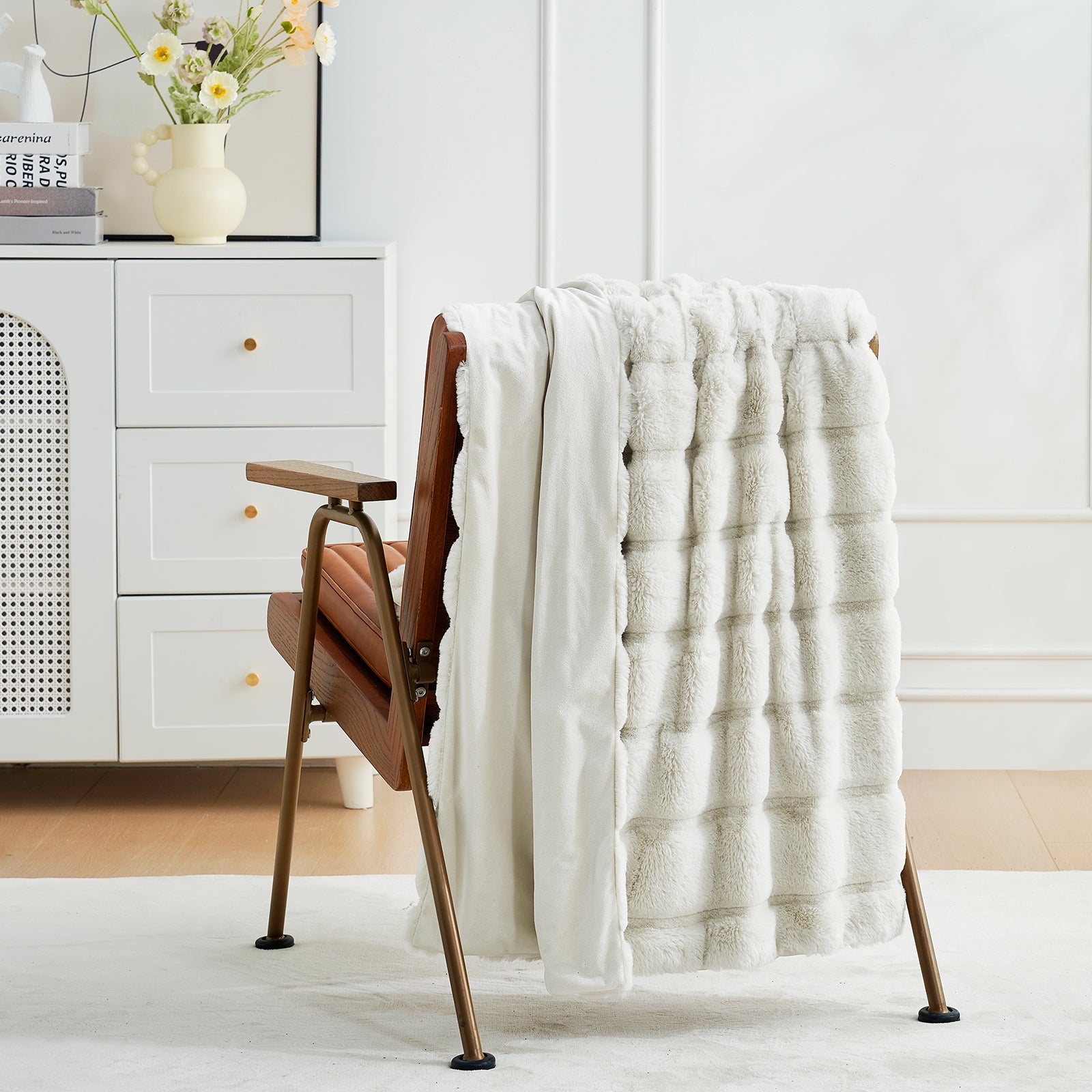 White textured blanket draped over a wooden chair in a room with a white dresser and decorative items. #color_Beige