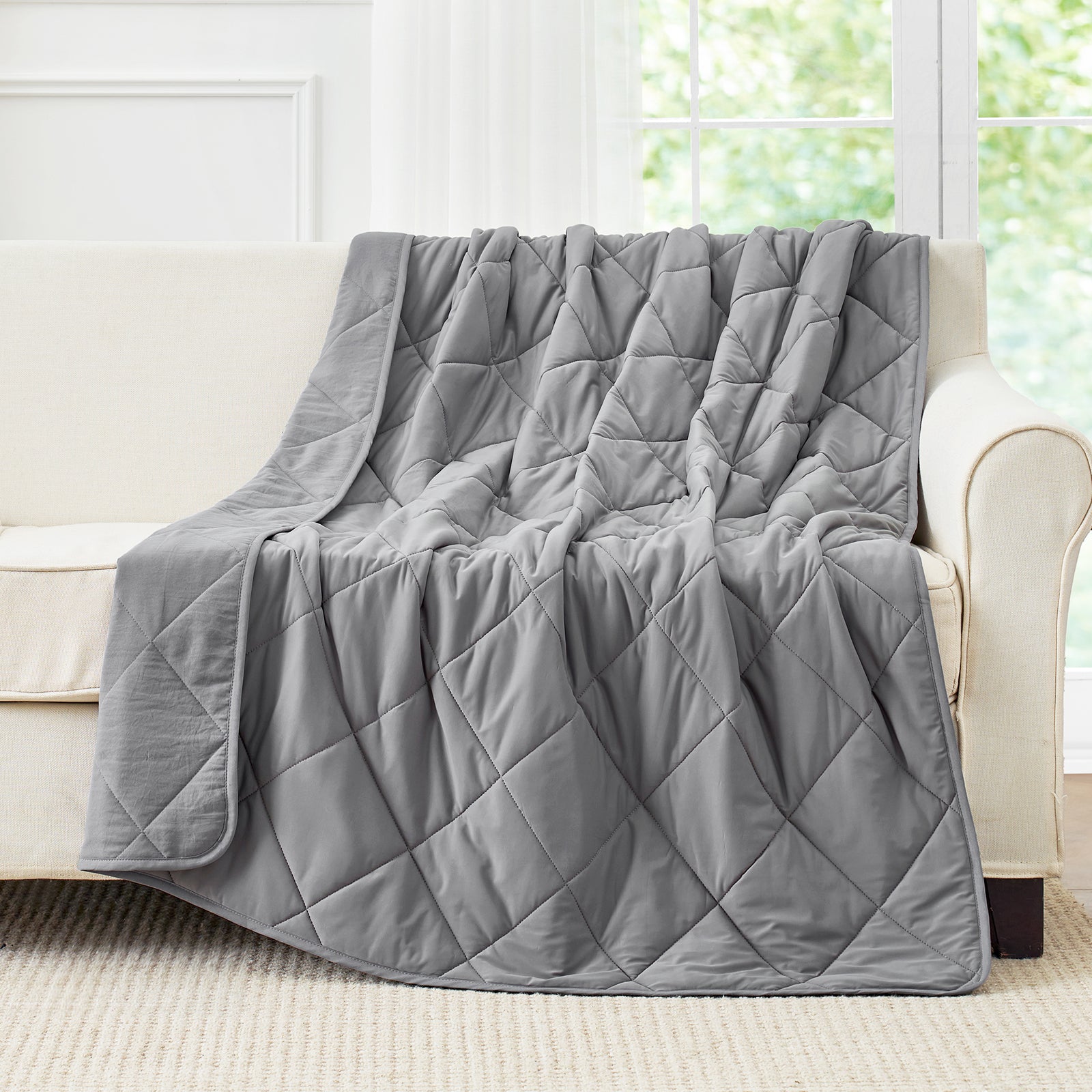 Gray cooling blanket draped over sofa, featuring diamond quilting pattern. Perfect for hot sleepers. #Color_Dark Grey