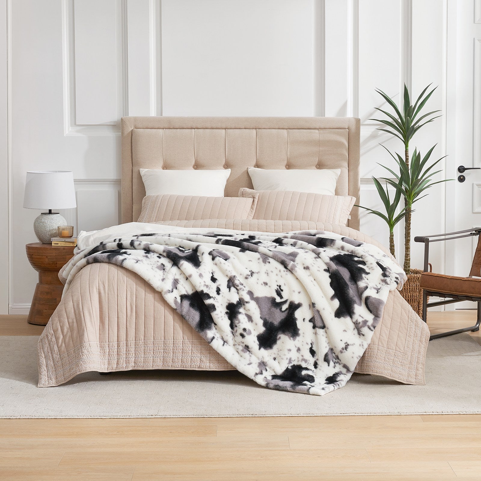 Cow print faux fur throw blanket draped on bed, cozy and soft, part of the Cozybliss collection. #color_Black/Grey