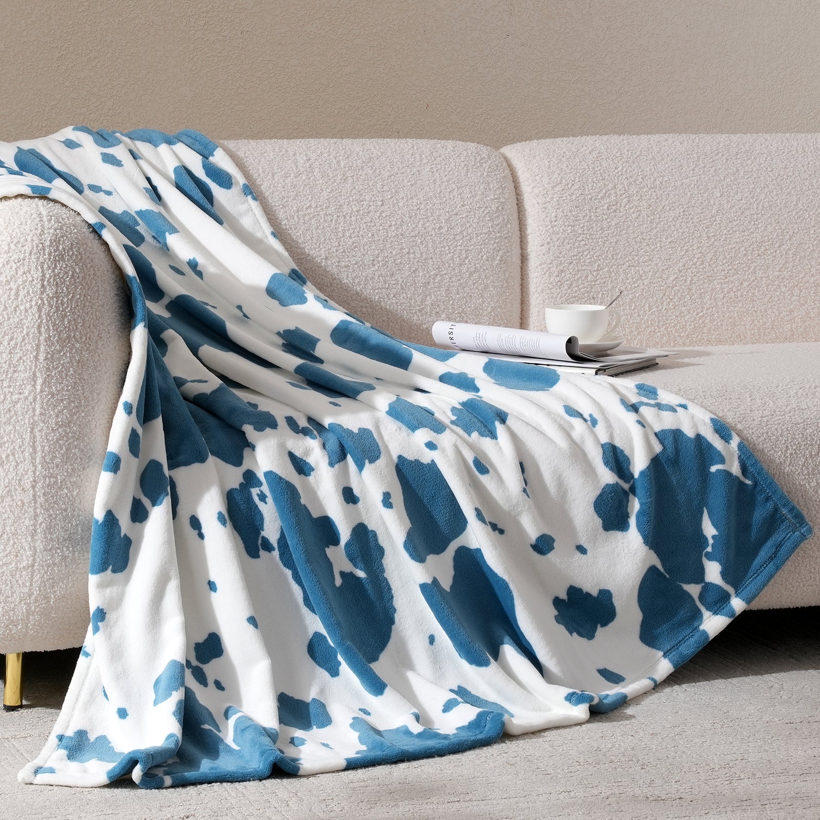 Blue and white patterned blanket draped over a beige sofa with a neutral background#color_Blue