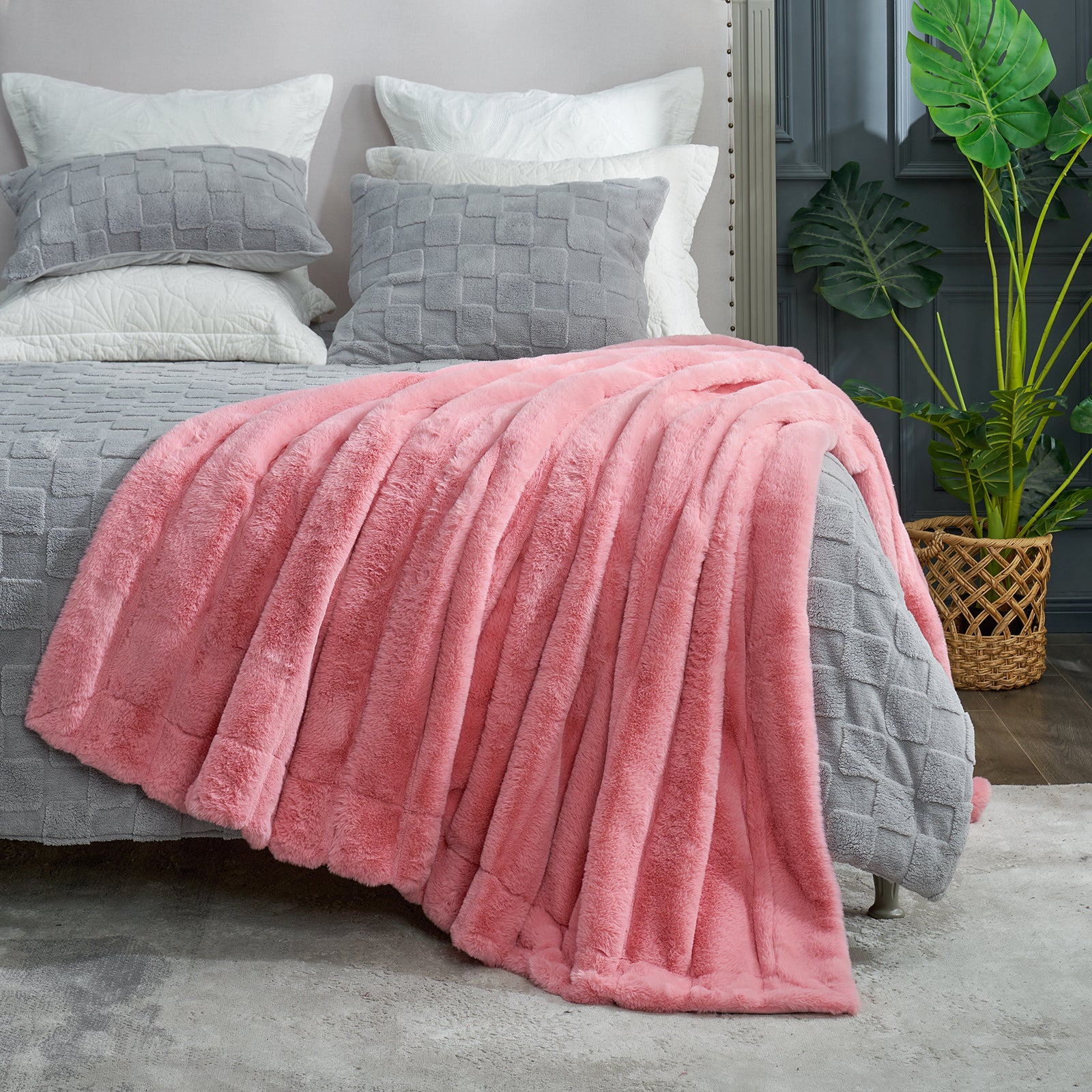 Pink blanket draped over a bed with gray and white pillows, plant in the background #color_Pink