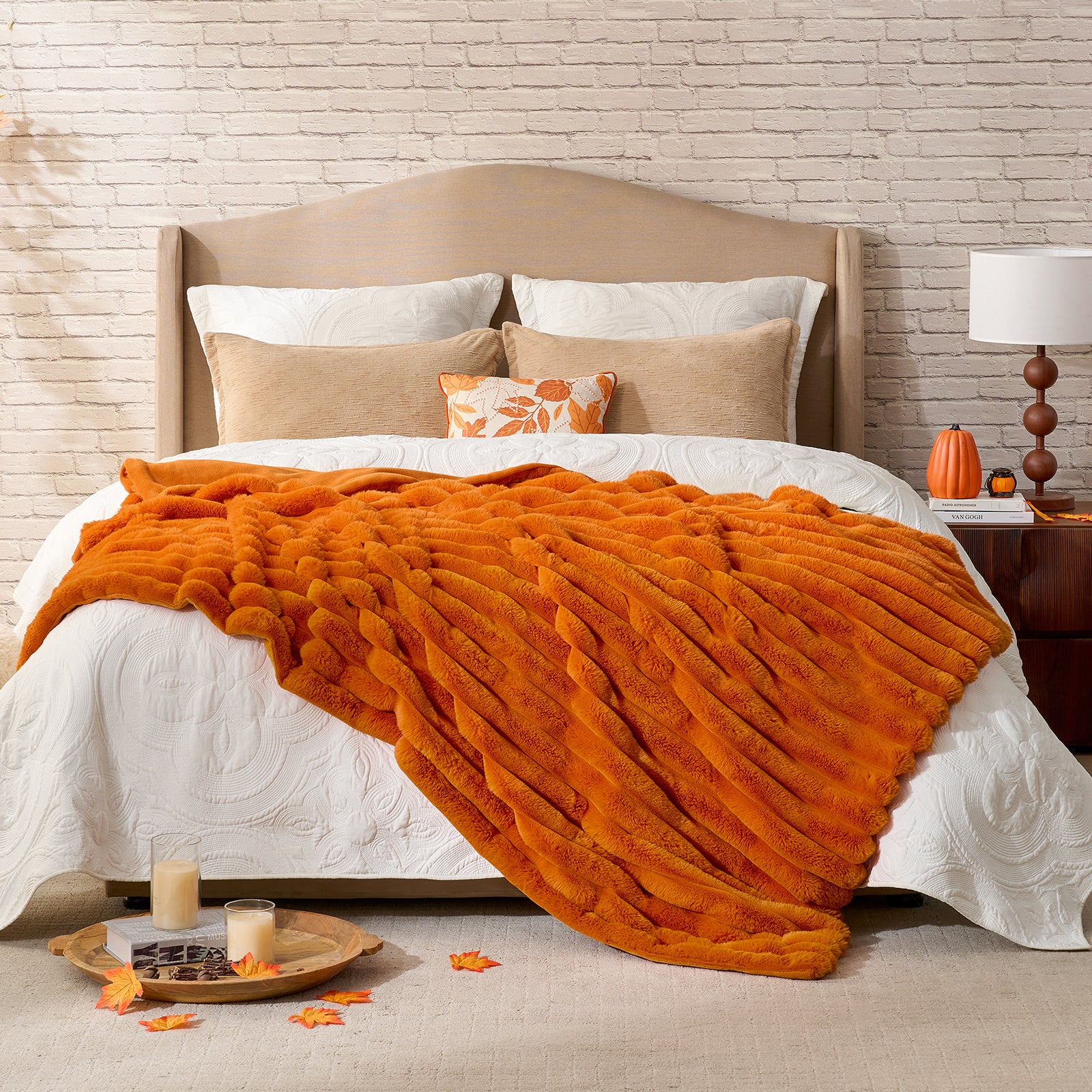 Orange blanket draped over a bed with pillows and a side table in a bedroom setting. #color_Burnt Orange