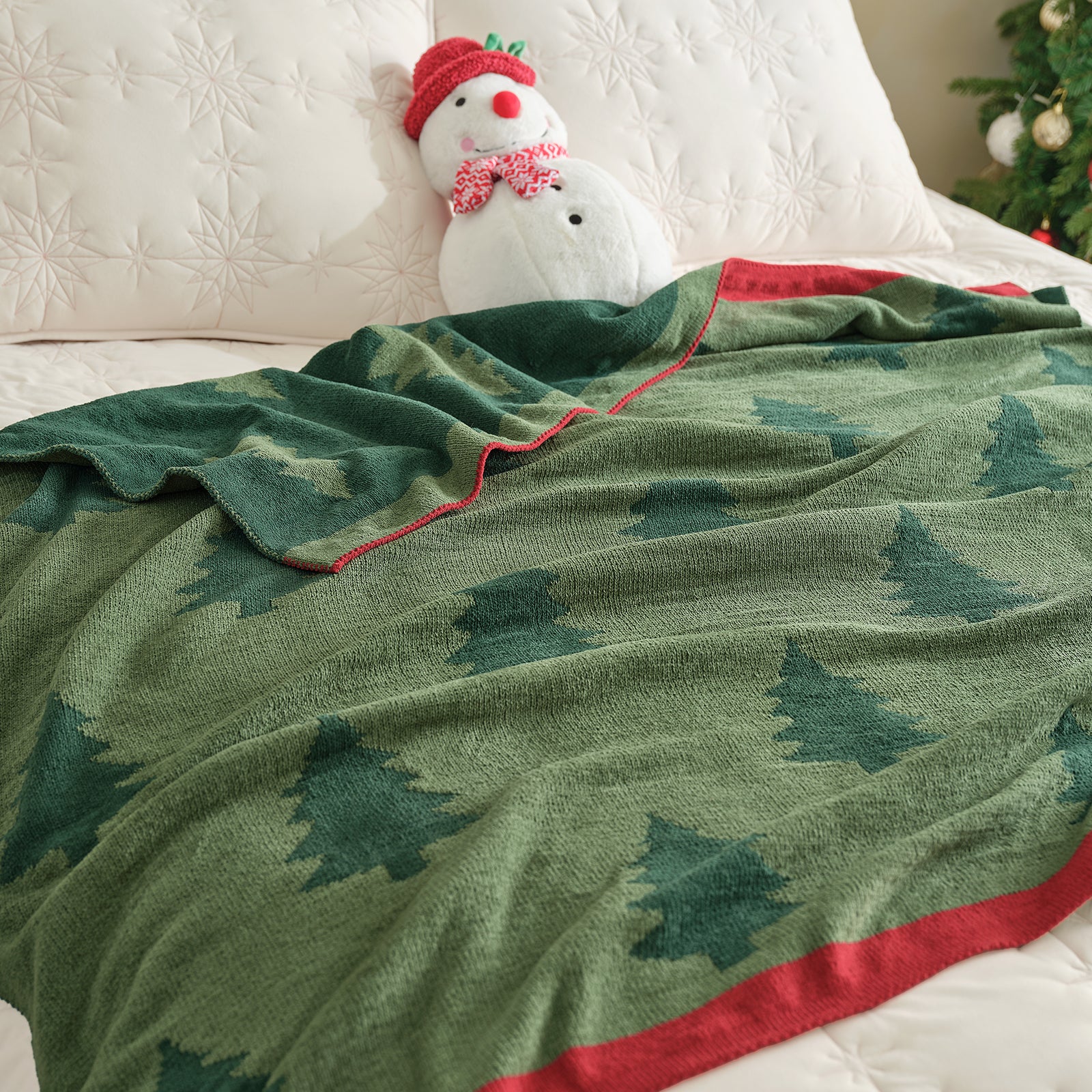 Green blanket with tree pattern draped over a bed, with a snowman toy in the background. #color_Christmas Tree