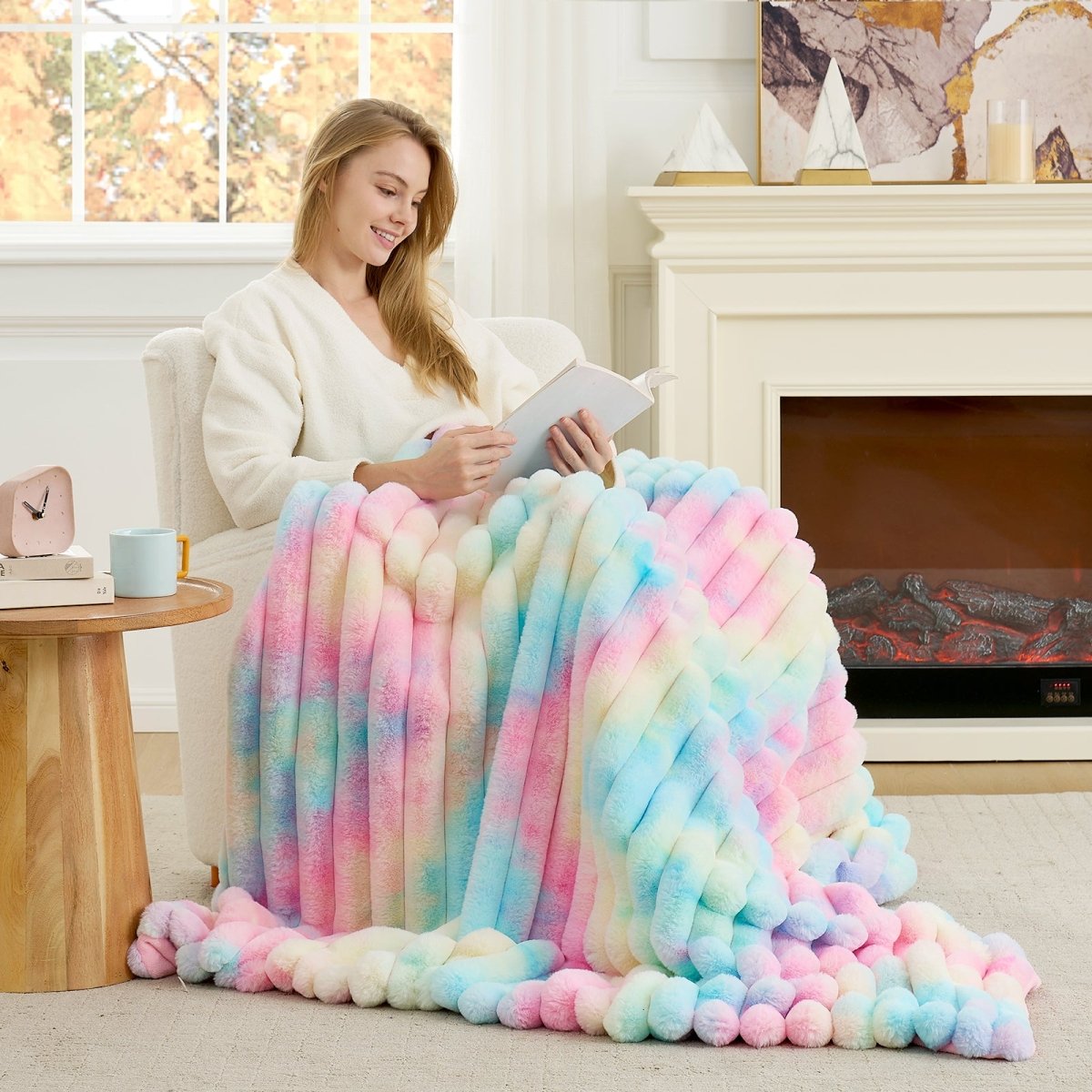Woman sitting on a couch with a colorful blanket, reading a book in a cozy living room. #color_Tie-dye Rainbow
