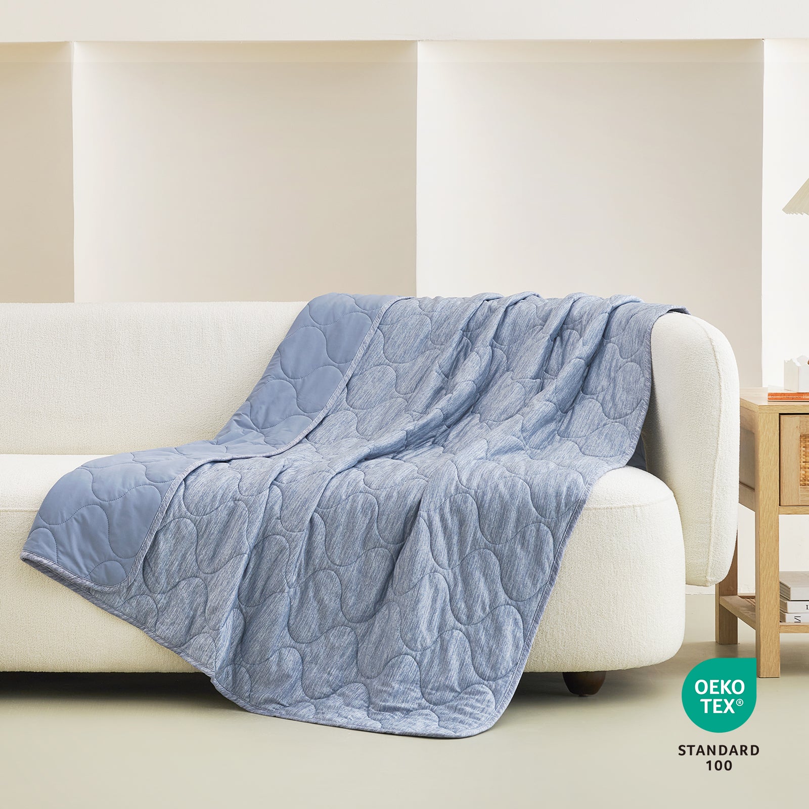 Cozy Bliss blue cooling blanket with cloud pattern on a white sofa, OEKO-TEX certified for cozy sleep. #color_Denim Blue