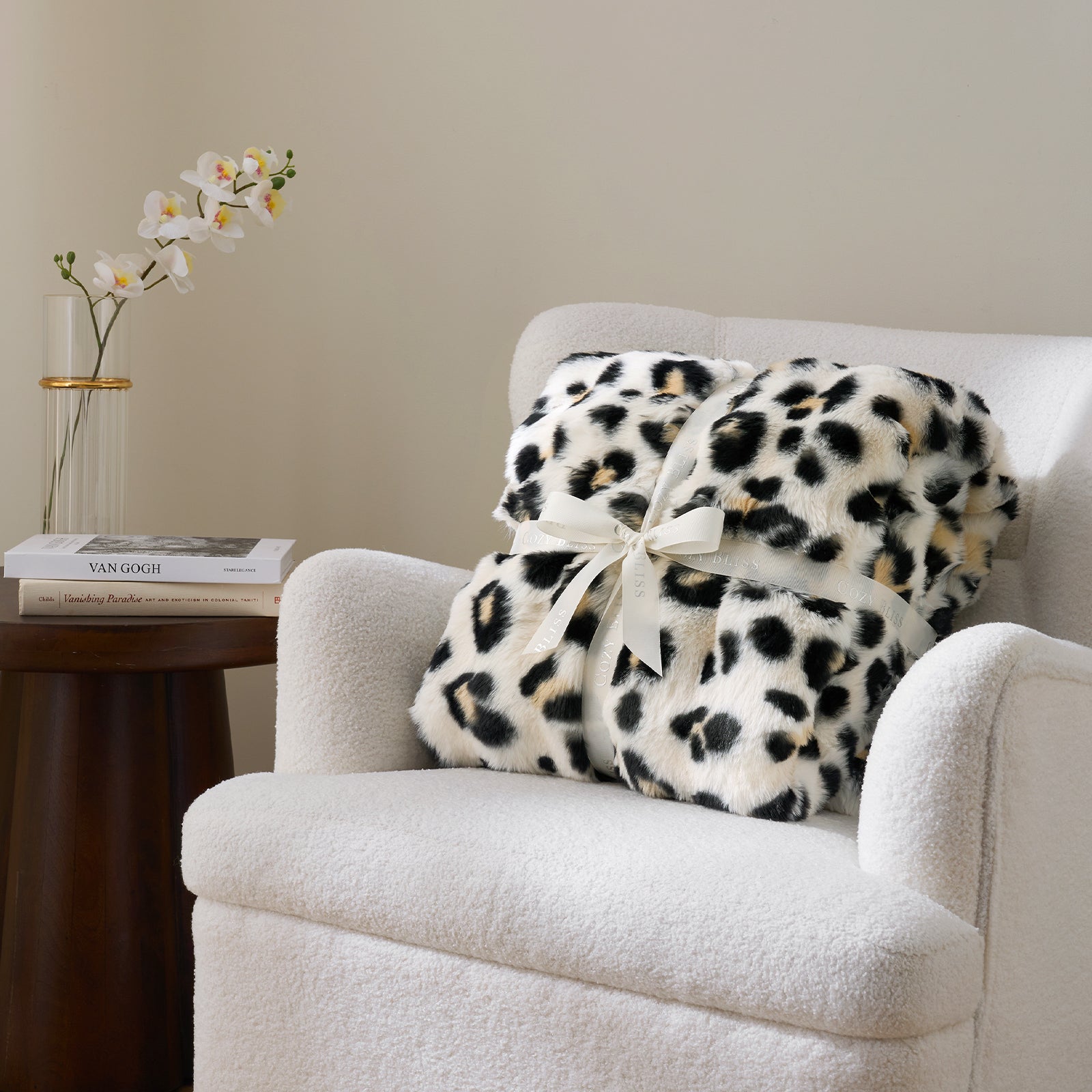 Leopard print blanket with a bow on a white armchair next to a side table with books and flowers. #Color_Leopard