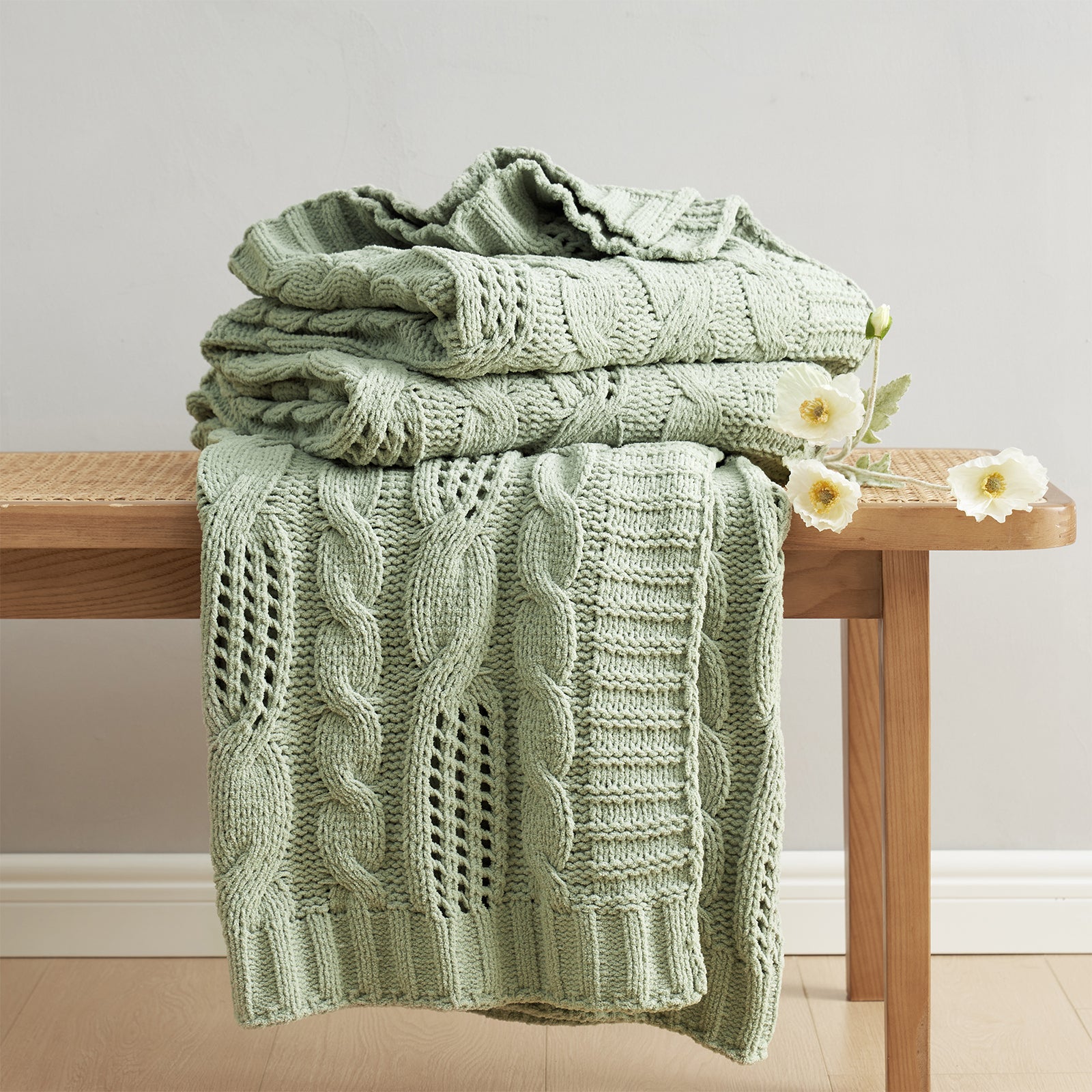 Chenille Cable Knit Throw Blanket in Sage Green neatly folded on a table, showcasing detailed cable knit pattern and soft chenille yarn. #color_Sage Green