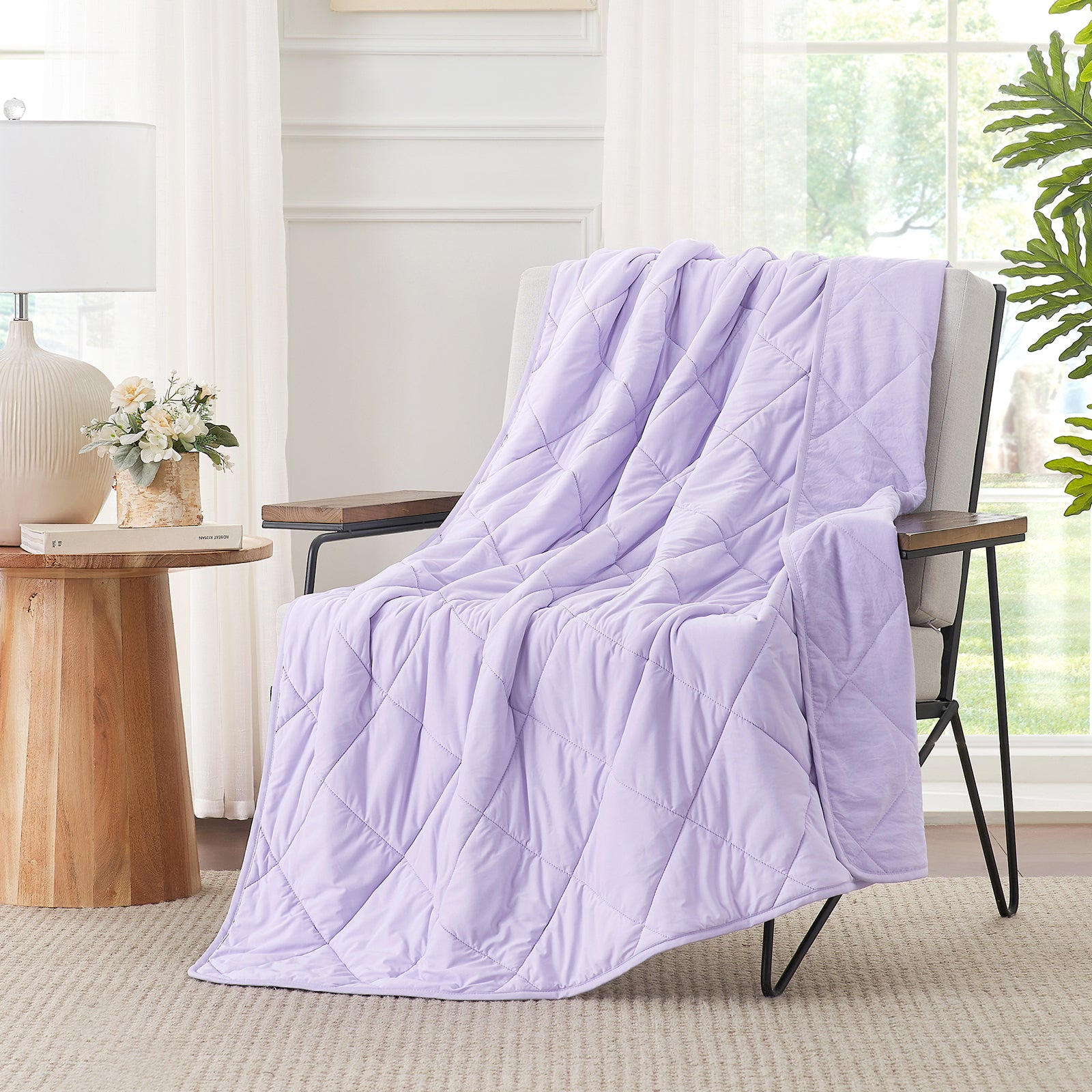 Light purple quilt draped over a chair in a bright room with a lamp and plant. #color_Purple