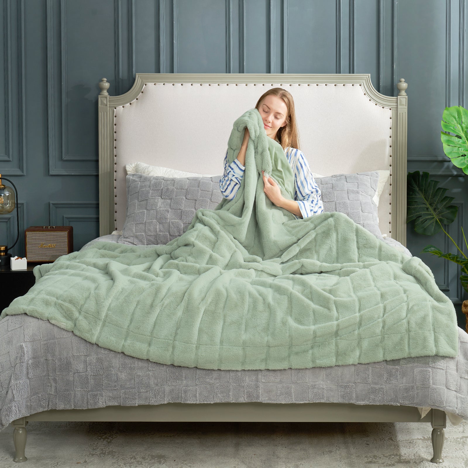 Woman wrapped in a green blanket on a bed with a gray headboard. #color_Sage Green