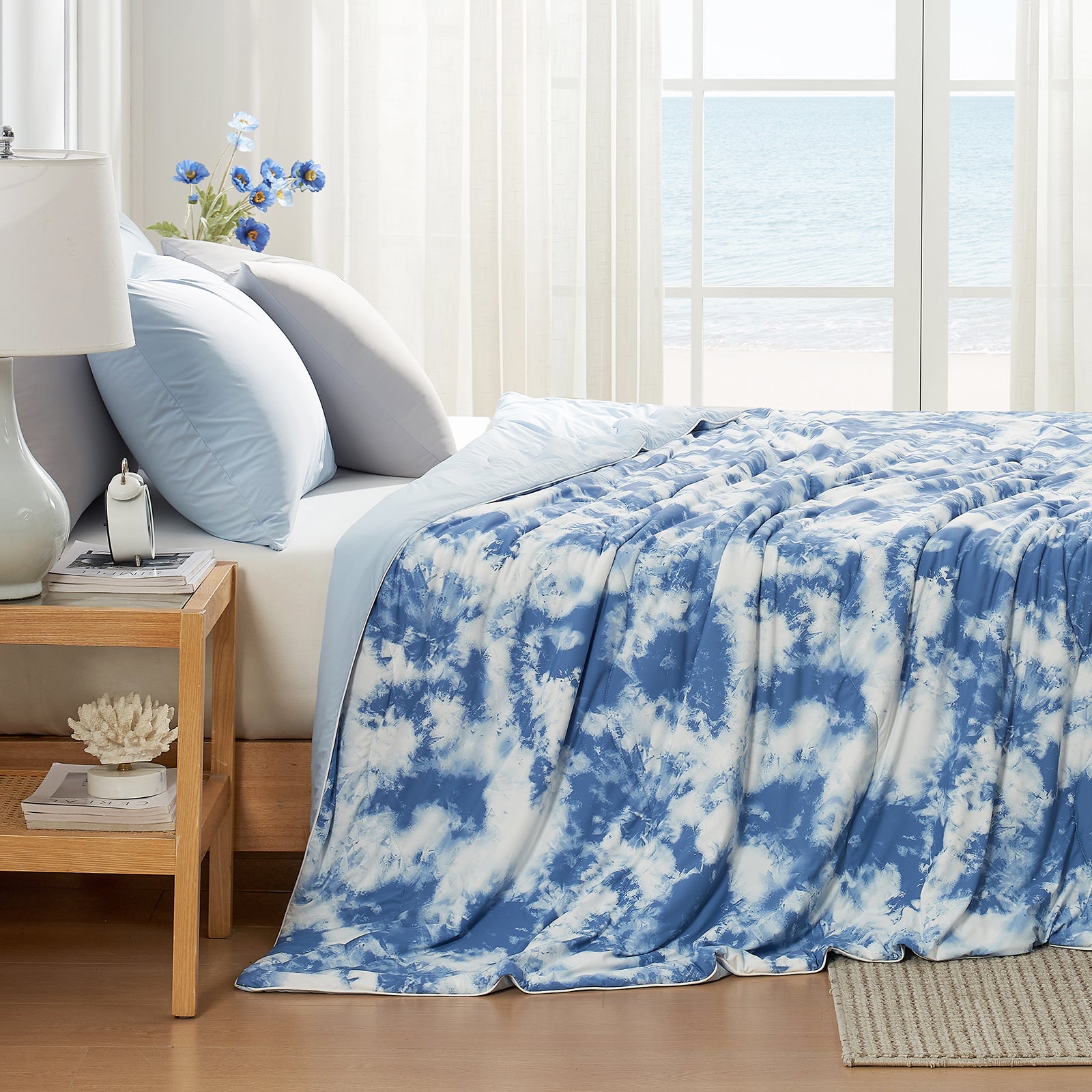 Blue and white tie-dye blanket on a bed in a bright bedroom with a window view. #Color_Tie-dye Blue