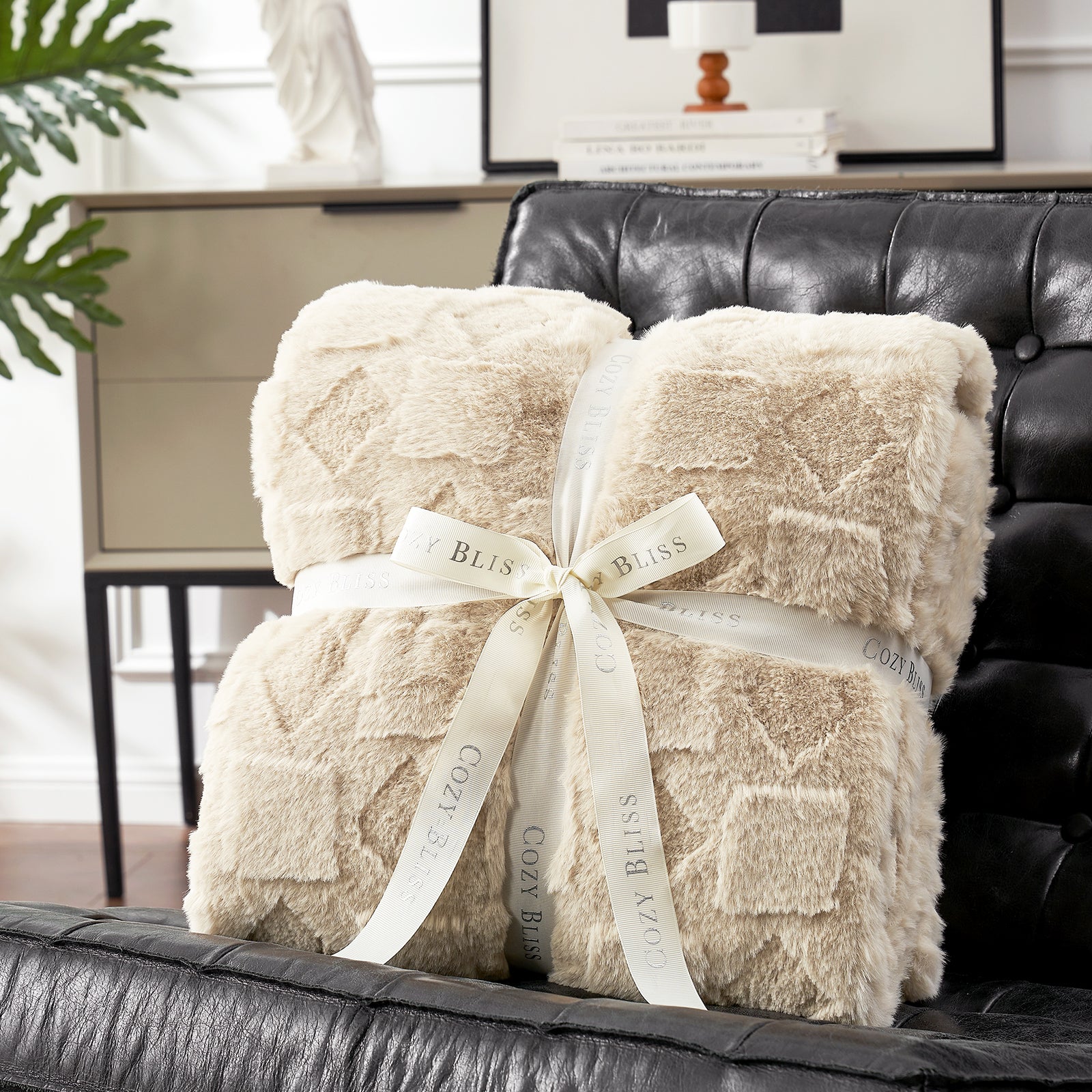 Two beige textured blankets tied with a white ribbon on a black leather couch.#color_Beige