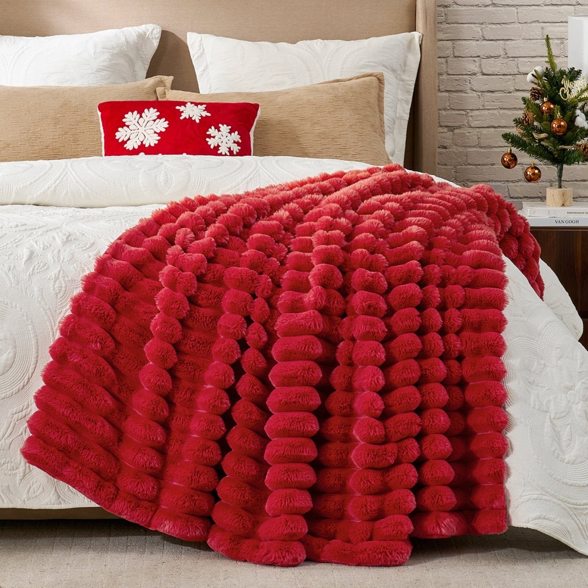 Red textured blanket on a bed with decorative pillows and a small Christmas tree in the background. #color_Christmas Red